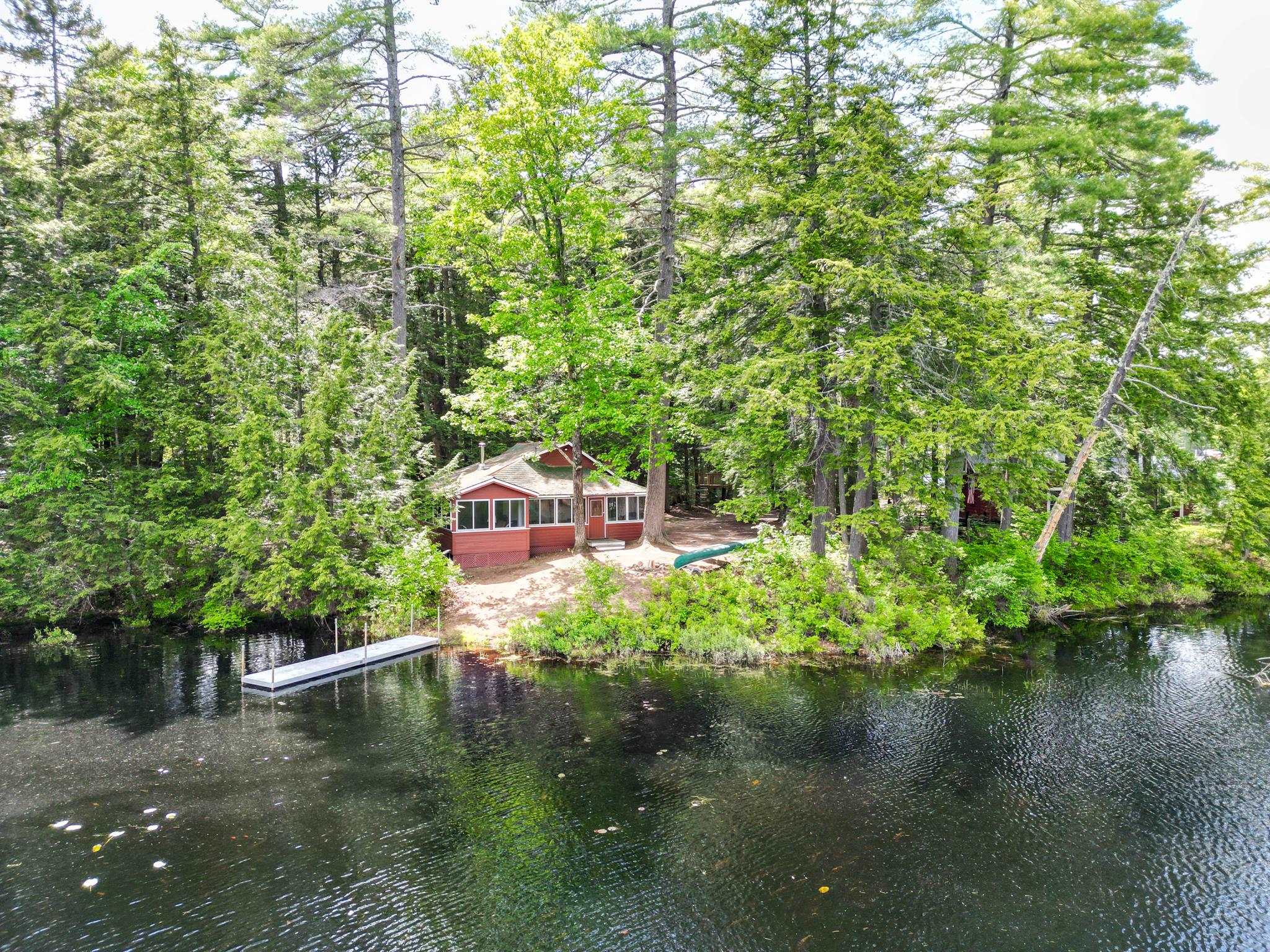 Red cottage among trees beside a river, with a small dock extending into the water.