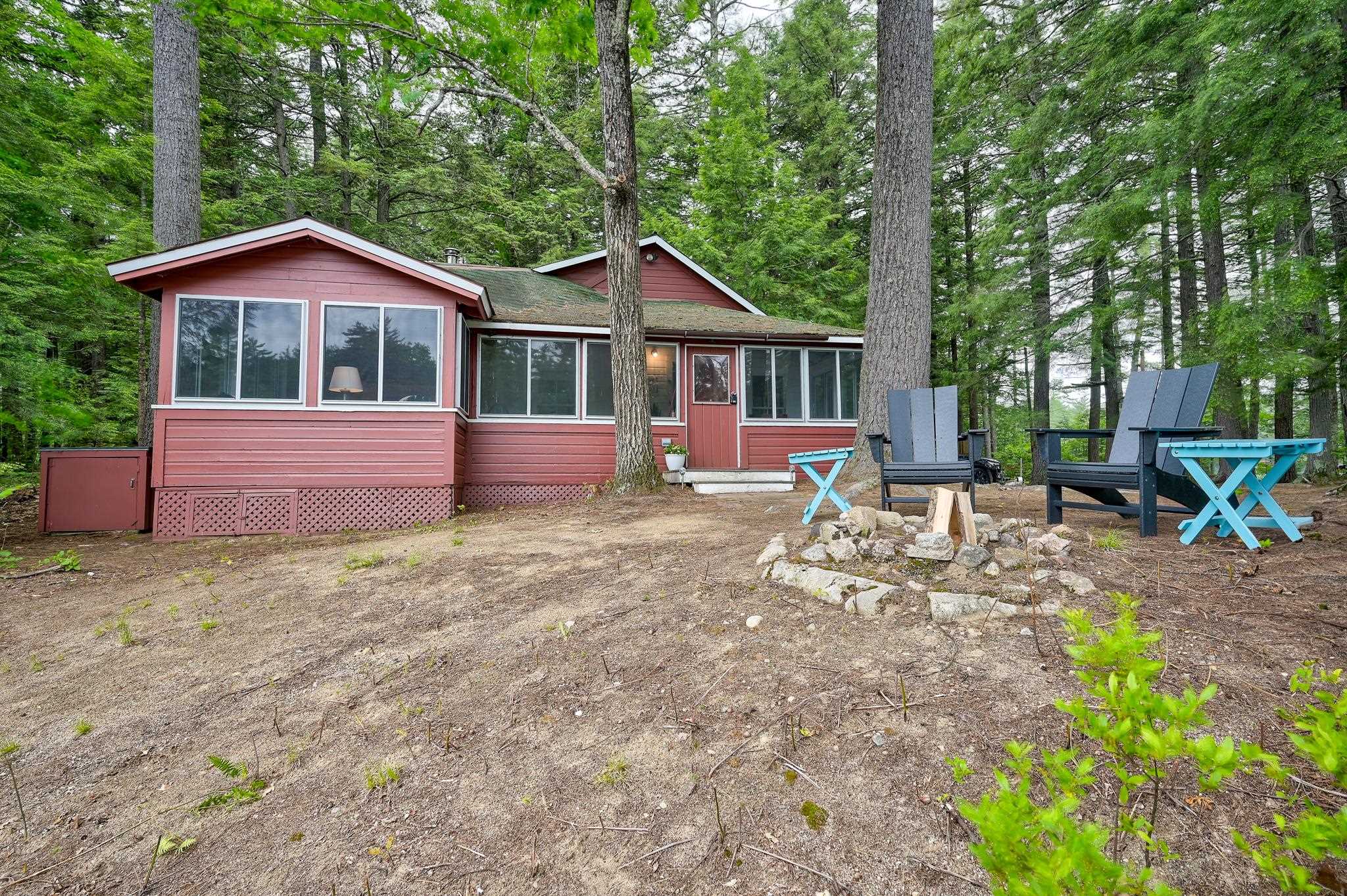 Red single-story home among trees, with wide windows and Adirondack chairs around a stone fire pit.