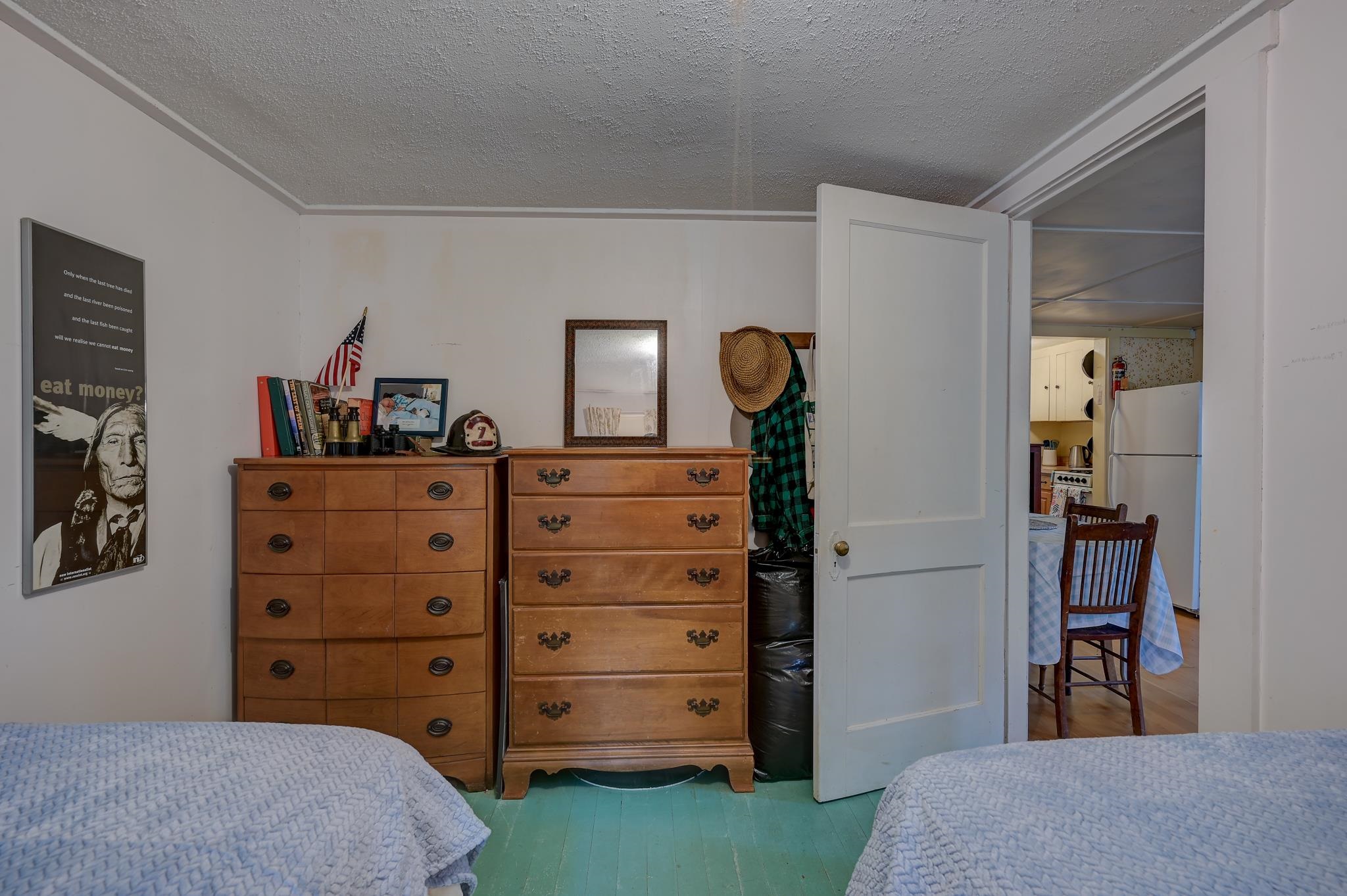 Furnished bedroom with two wooden dressers and an open doorway to the kitchen and dining area.