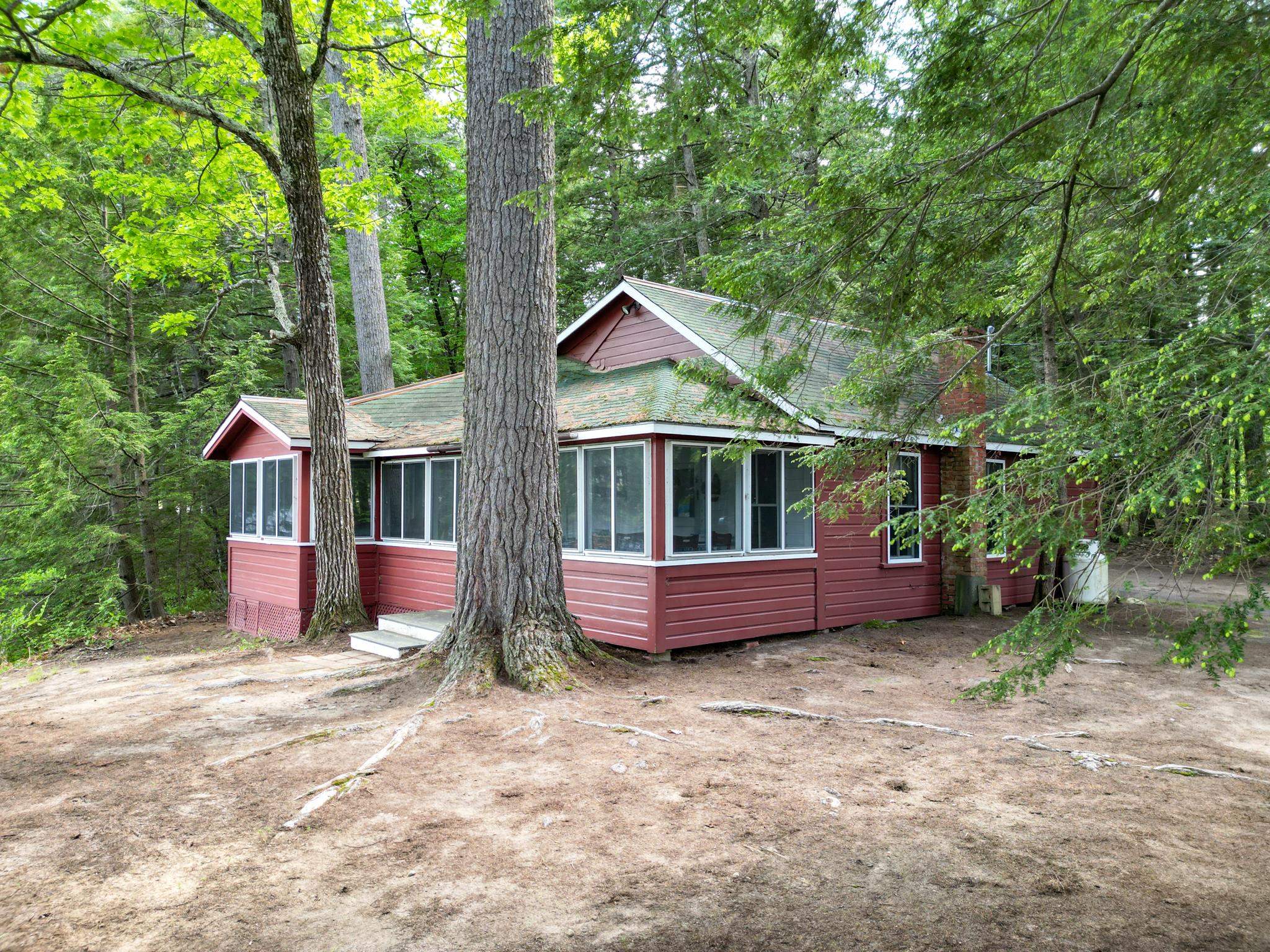 Red home with broad windows nestled among mature trees in a wooded yard.