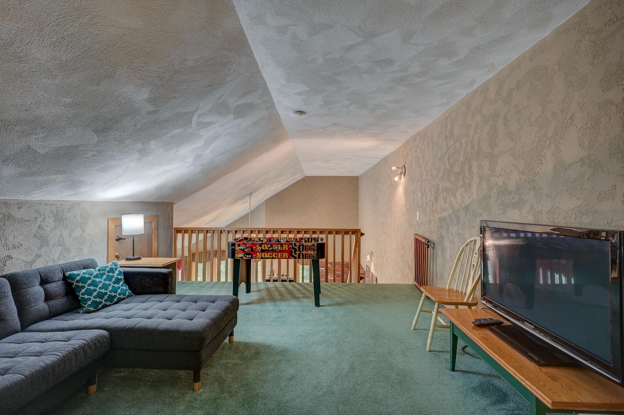 Furnished loft recreation area with a gray sectional, foosball table, and large television.