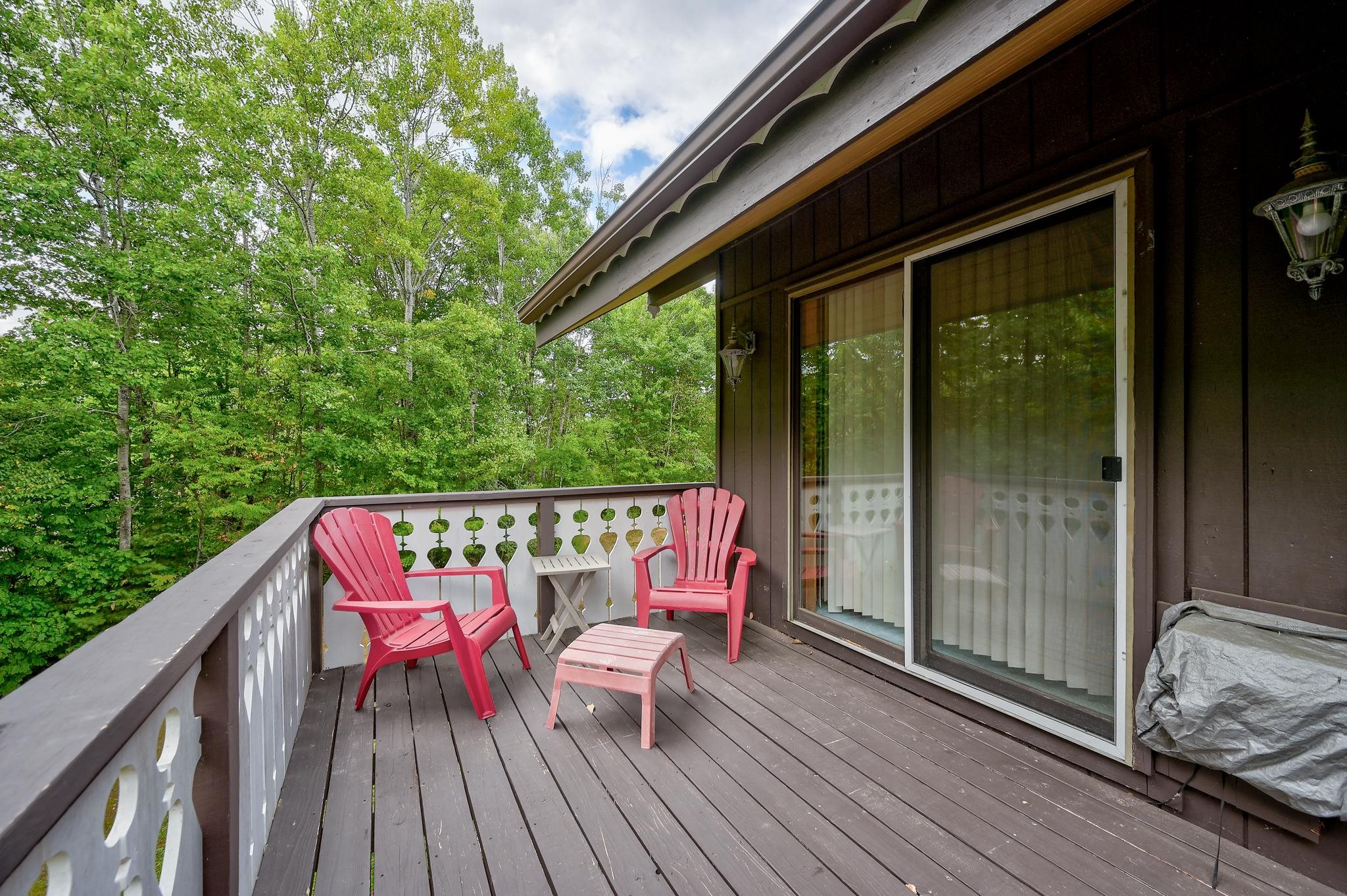 Wooden deck with pink Adirondack chairs overlooking leafy woods.