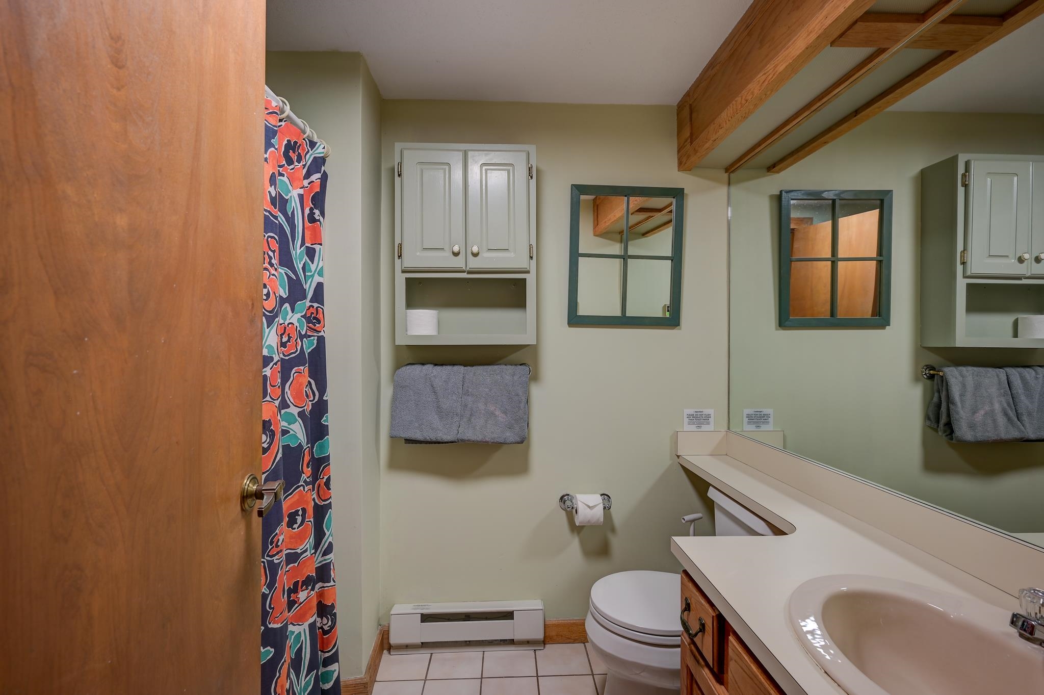 Bathroom with a long white vanity, patterned shower curtain, and exposed wooden ceiling beams.