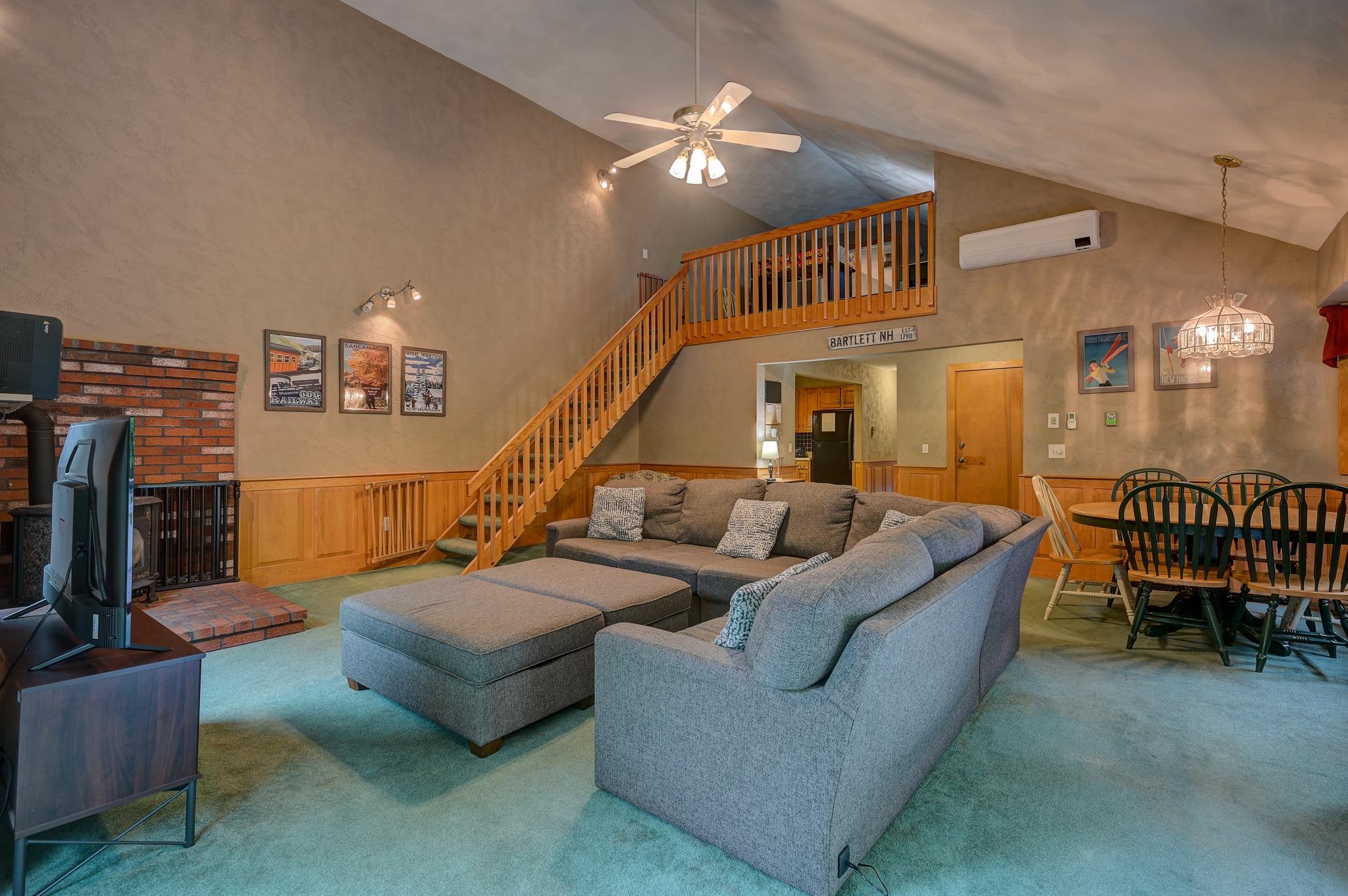Living room with a gray sectional, brick fireplace, dining area, and wooden staircase to a loft.