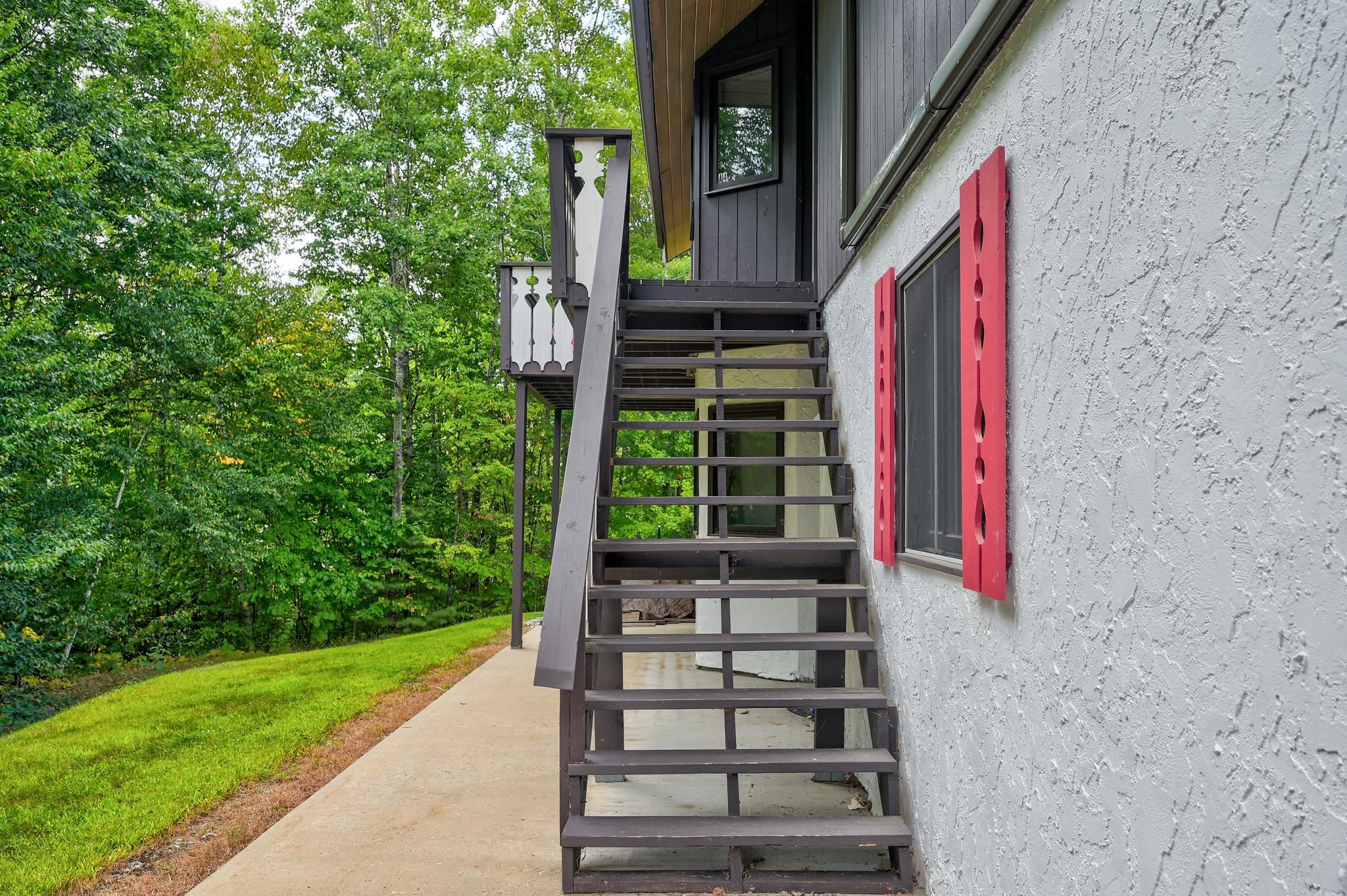 Home exterior with dark outdoor stairs, red shutters, and a leafy wooded setting.
