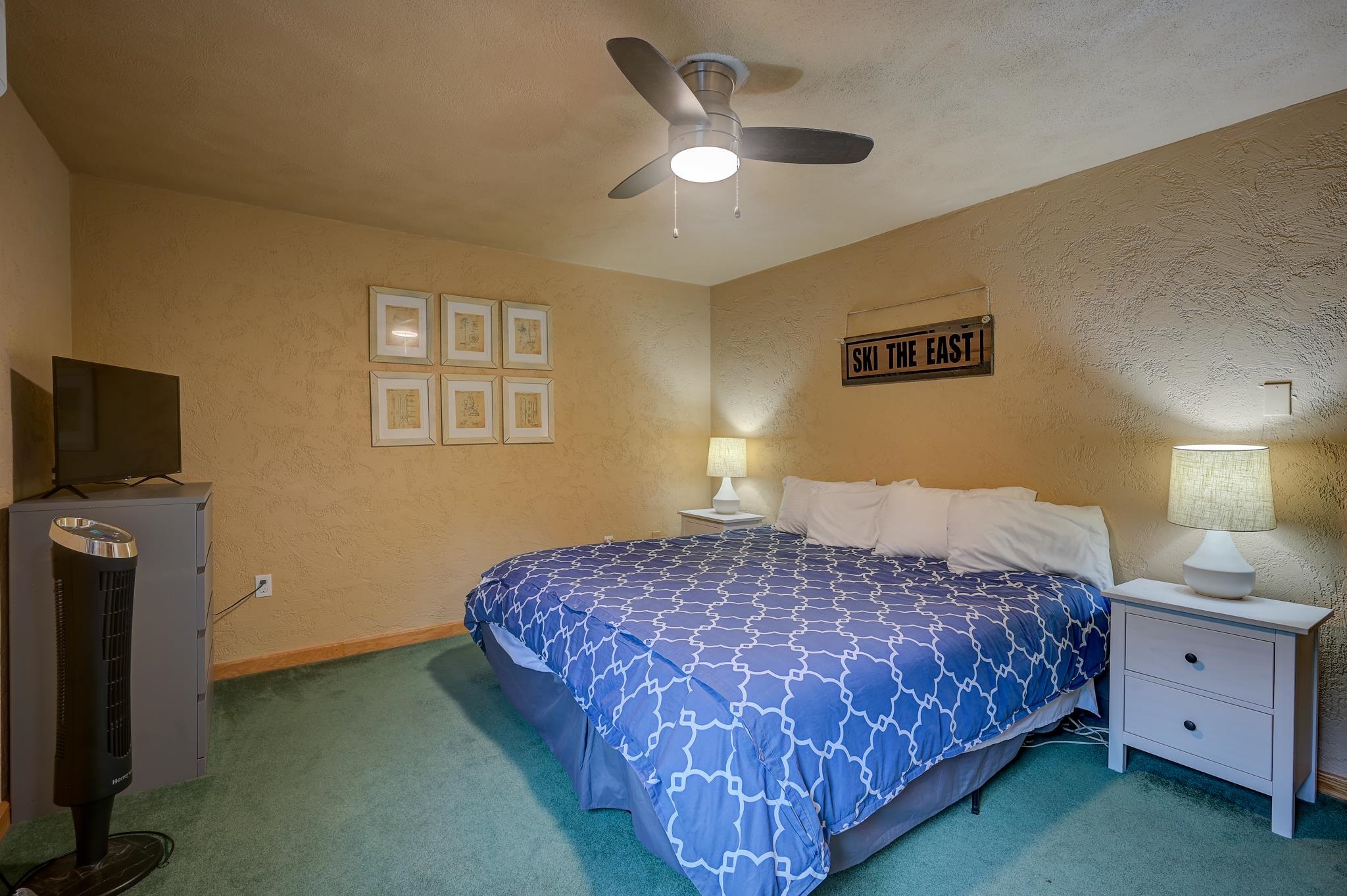 Bedroom with blue patterned bedding, bedside lamps, a television, and a ceiling fan.