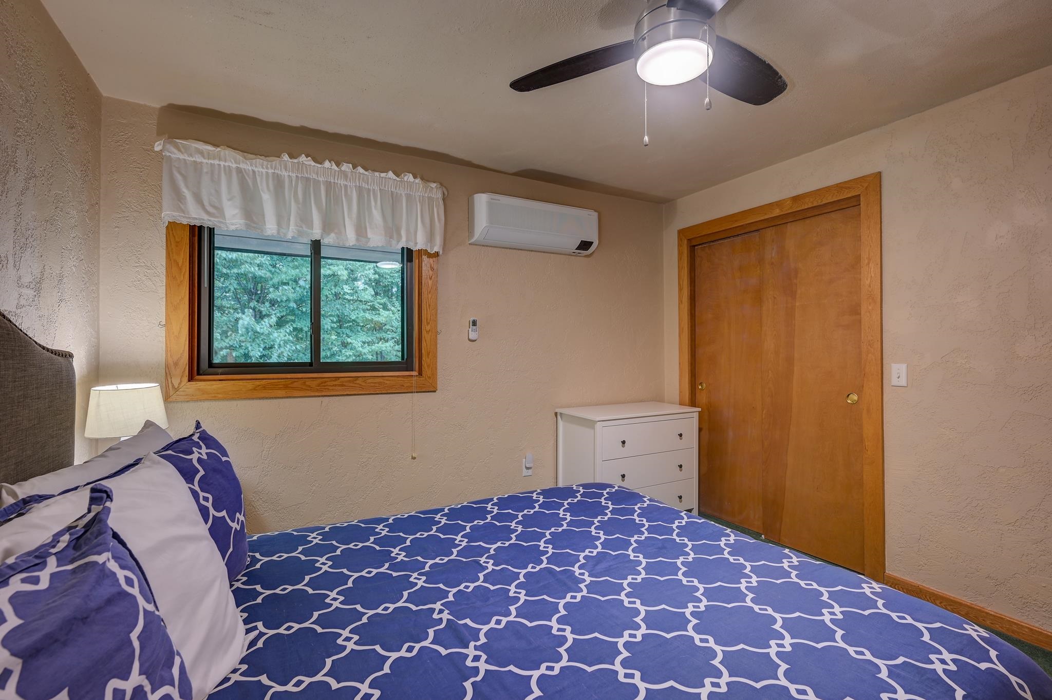 Bedroom with blue-and-white patterned bedding, a tree-facing window, and wooden closet doors.
