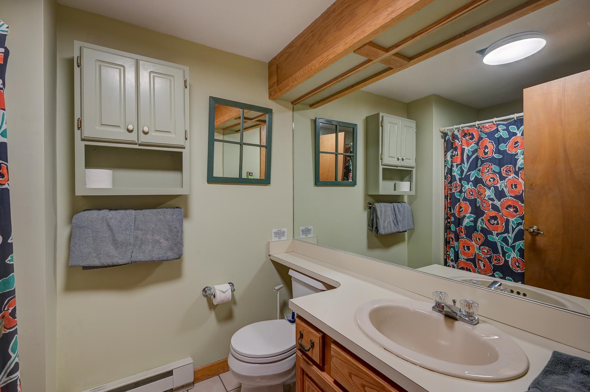 Bathroom with a long vanity, exposed ceiling beams, and a colorful floral shower curtain.