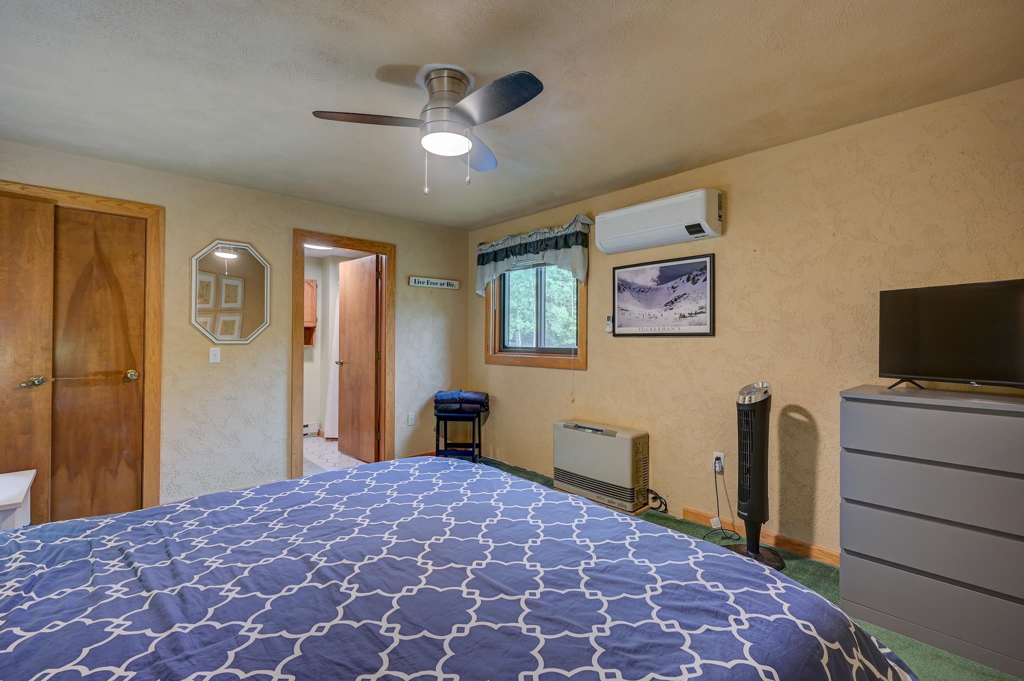 Furnished bedroom with a blue patterned bedspread, ceiling fan, and window air conditioner.