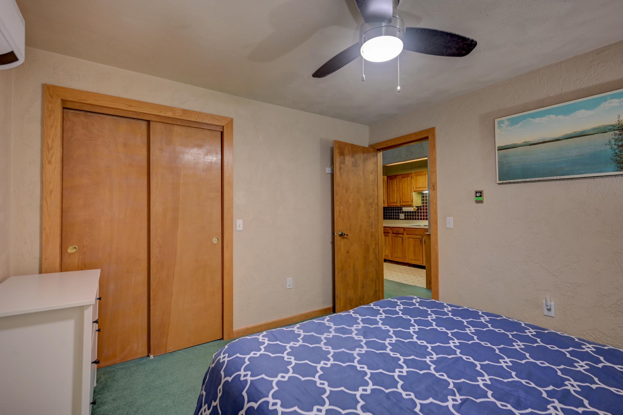 Bedroom with a blue patterned bedspread, wood closet doors, and an open doorway to the kitchen.