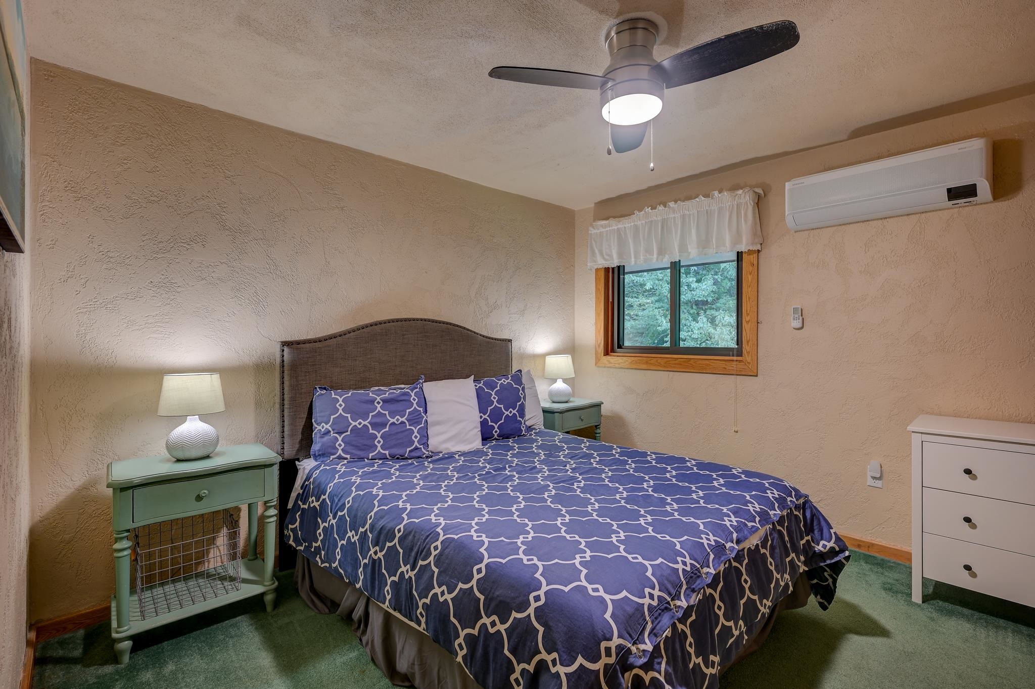 Bedroom with blue patterned bedding, green bedside tables, and a window overlooking trees.