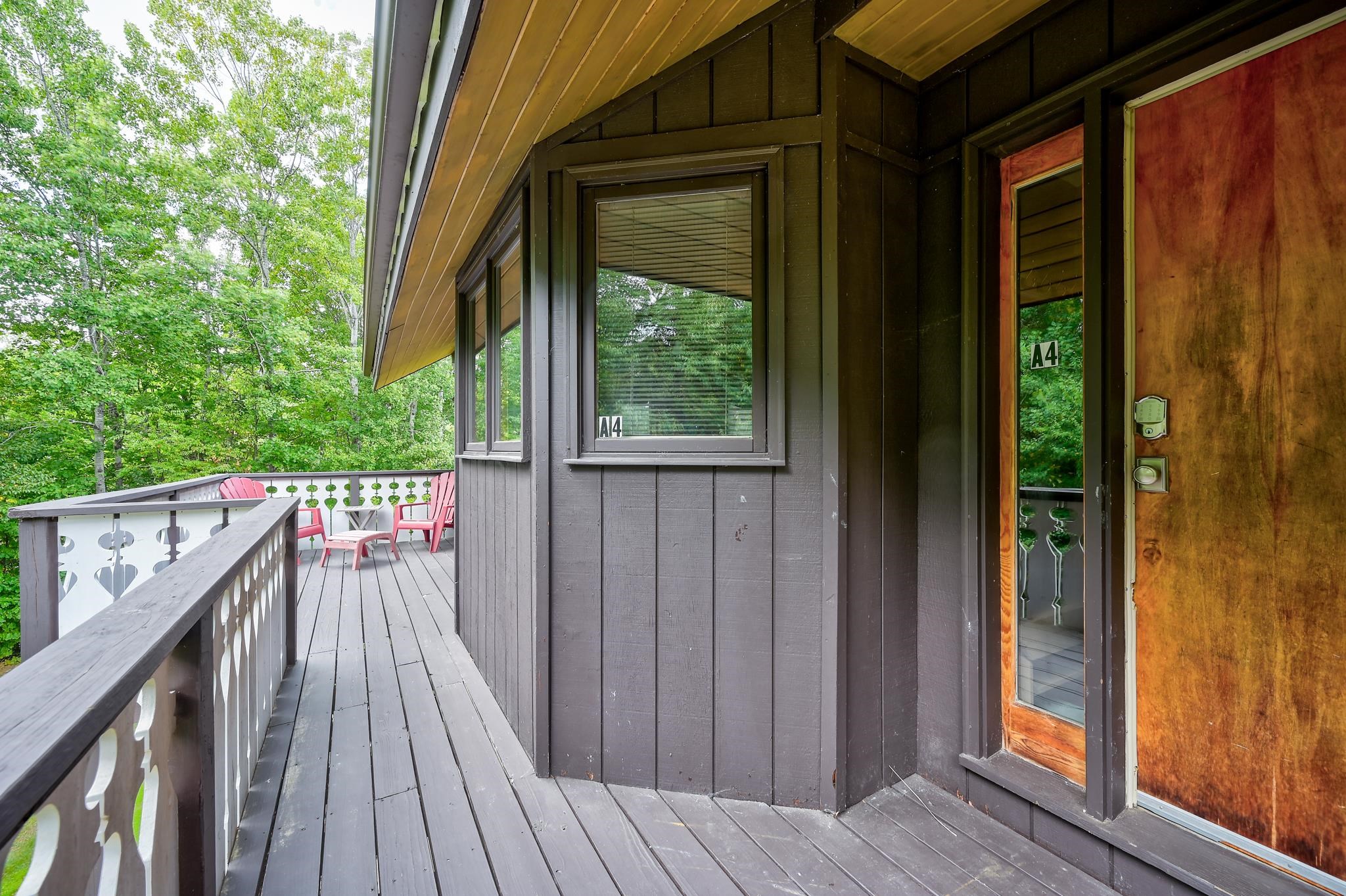 Unit A4 entrance and deck with decorative railings, pink chairs, and leafy trees.