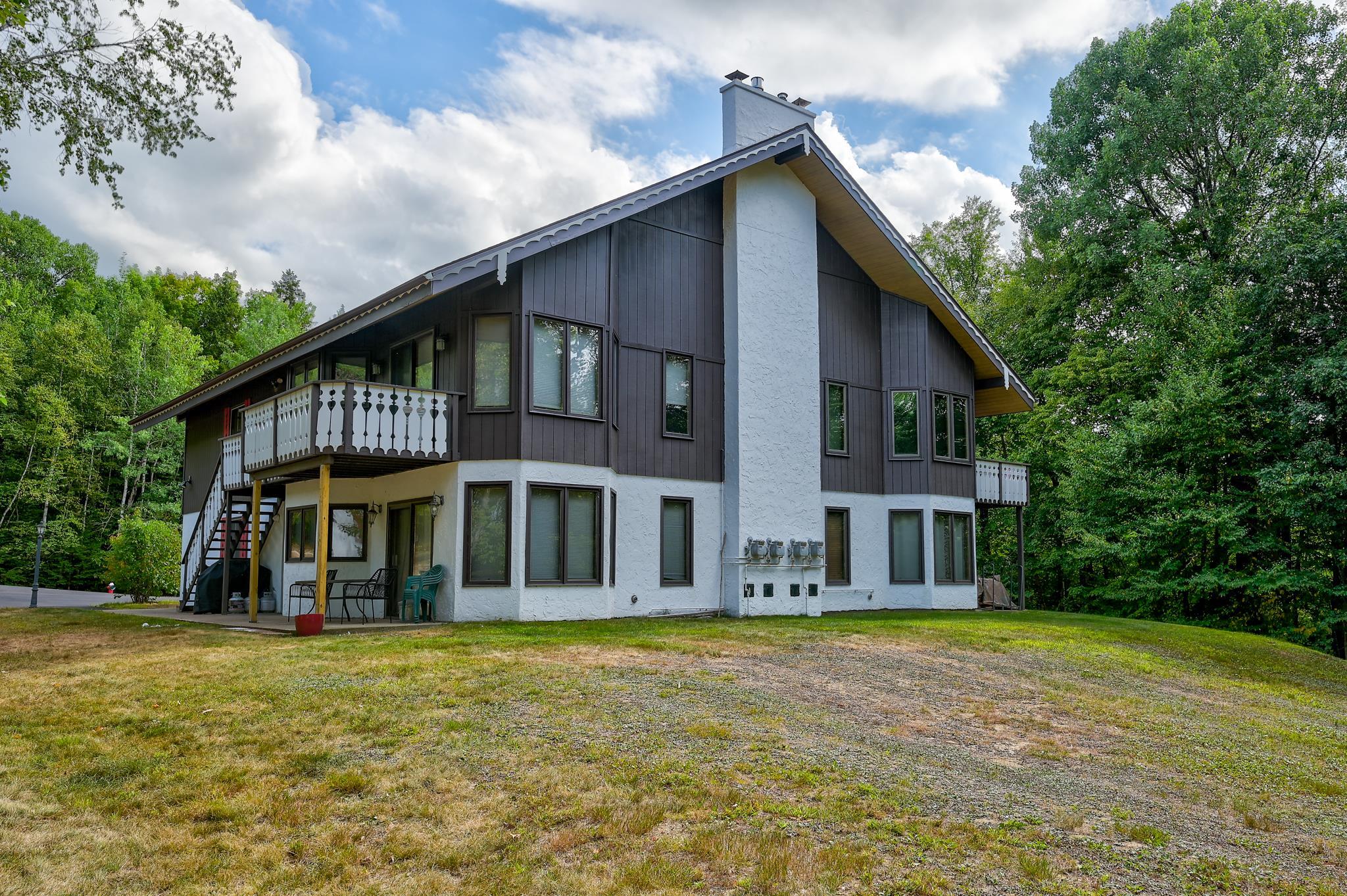 Condominium building with a steep gabled roof, two balconies, and wooded surroundings.