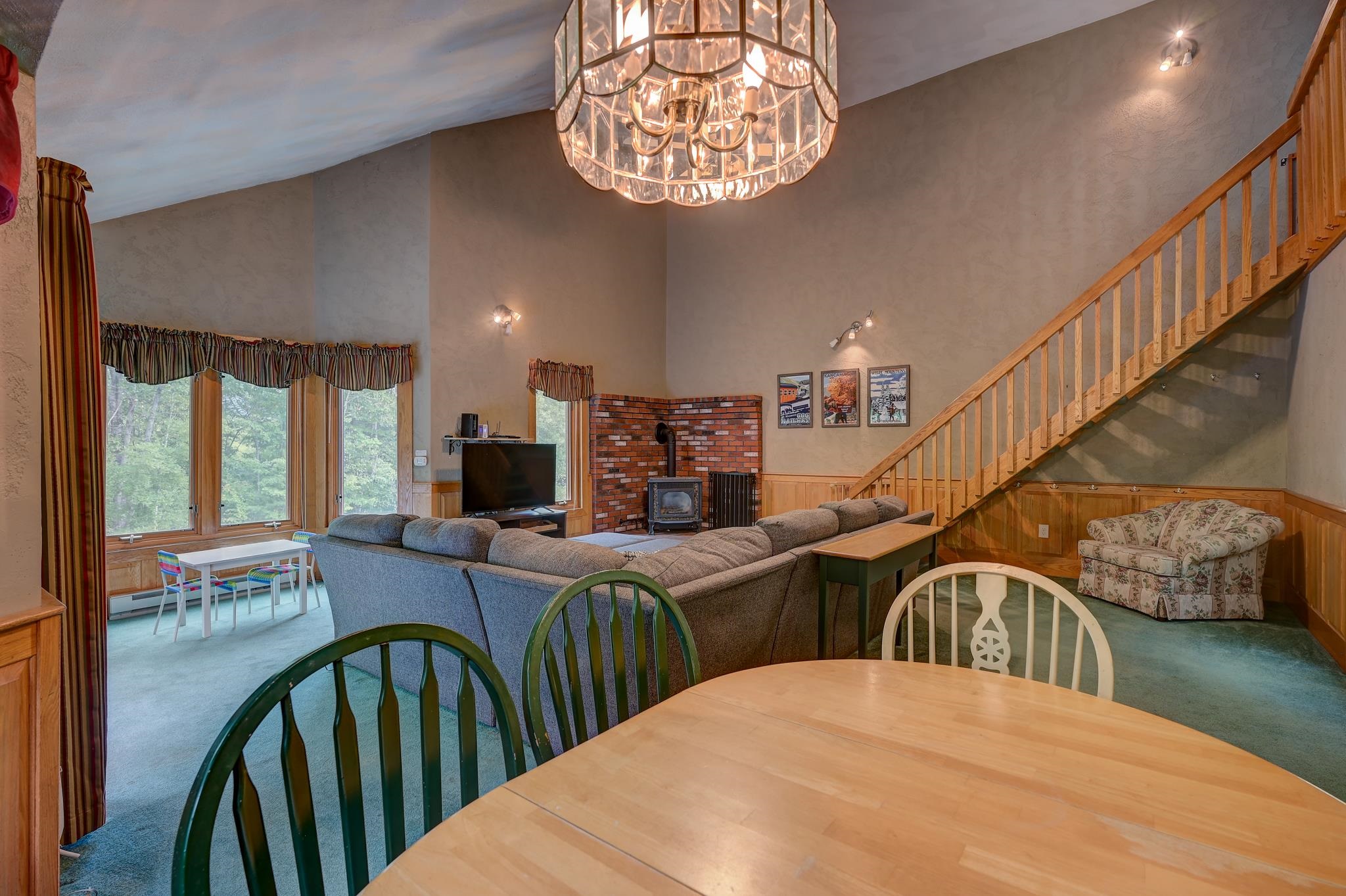 Living and dining area with a brick fireplace, sectional sofa, large chandelier, and staircase.