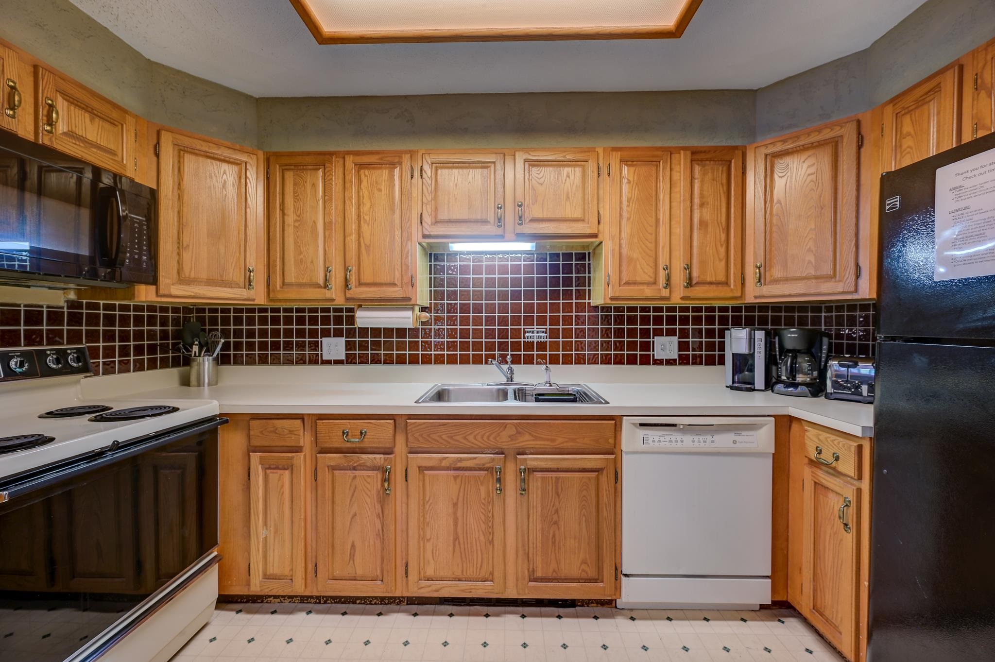 Kitchen with honey-toned wood cabinets, dark tiled backsplash, and a double-basin sink.