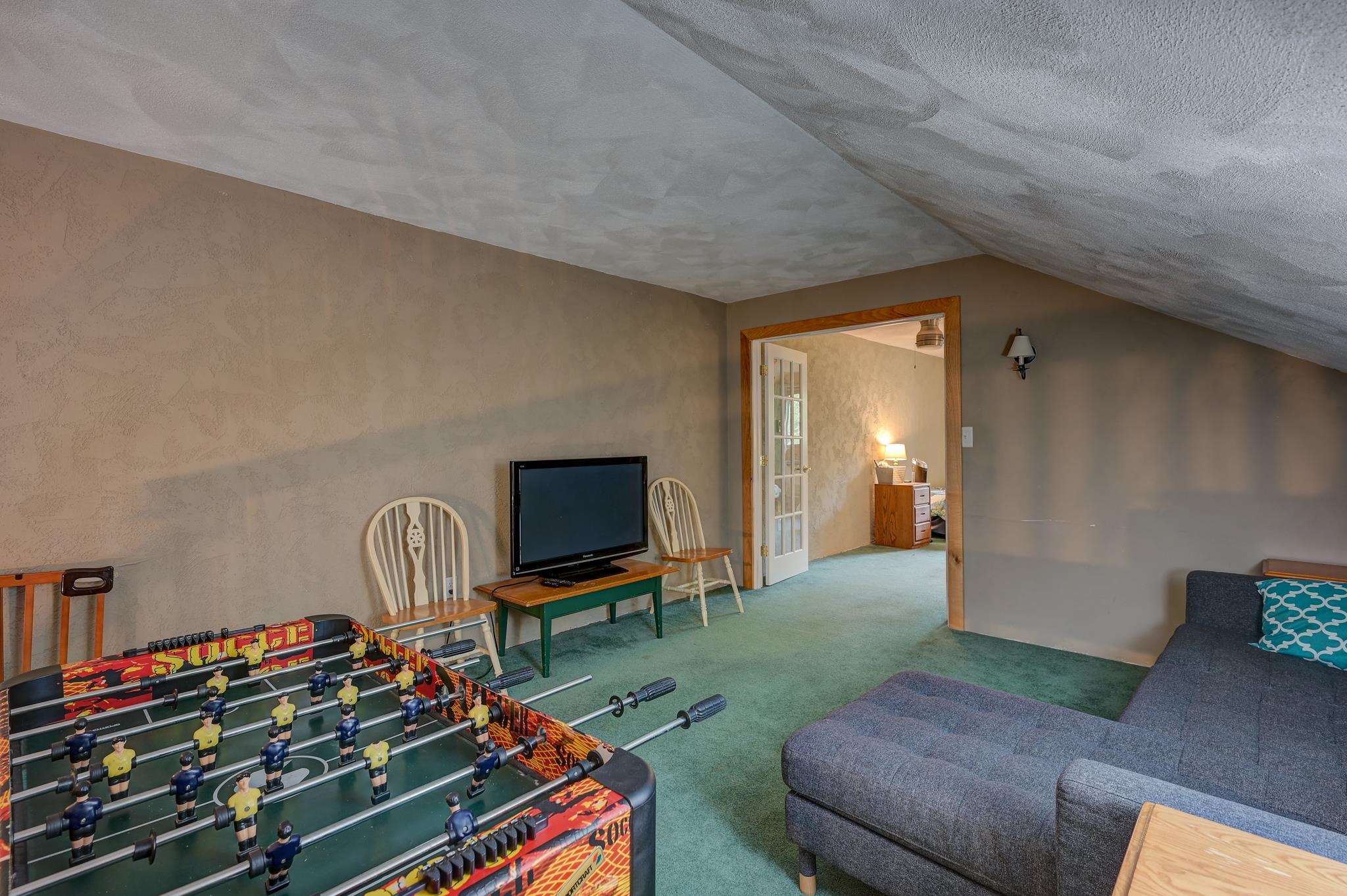 Furnished recreation room with a foosball table, television, and gray sectional under a sloped ceiling.