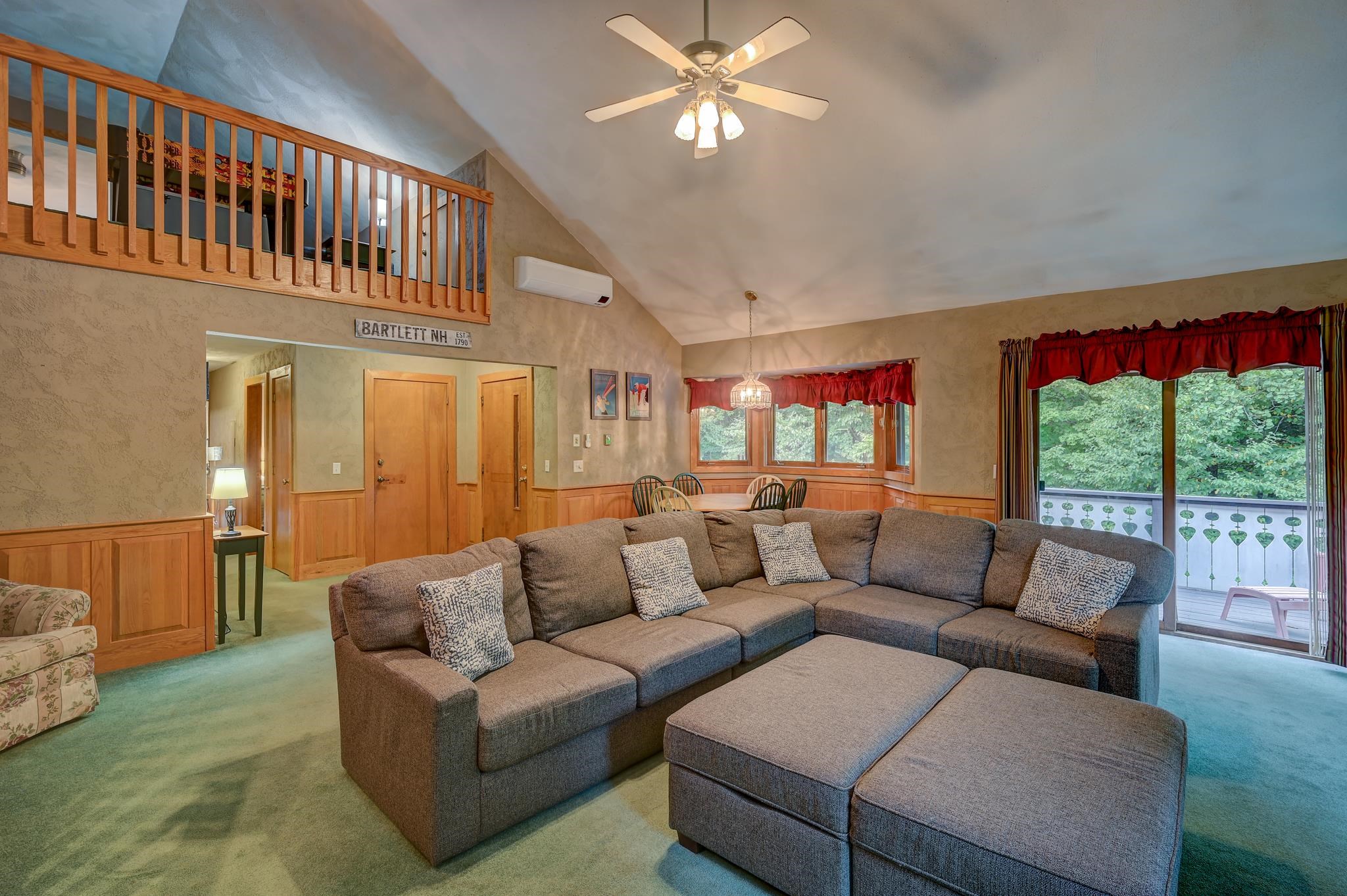 Living room with a large sectional, vaulted ceiling, wooden loft railing, and balcony doors.