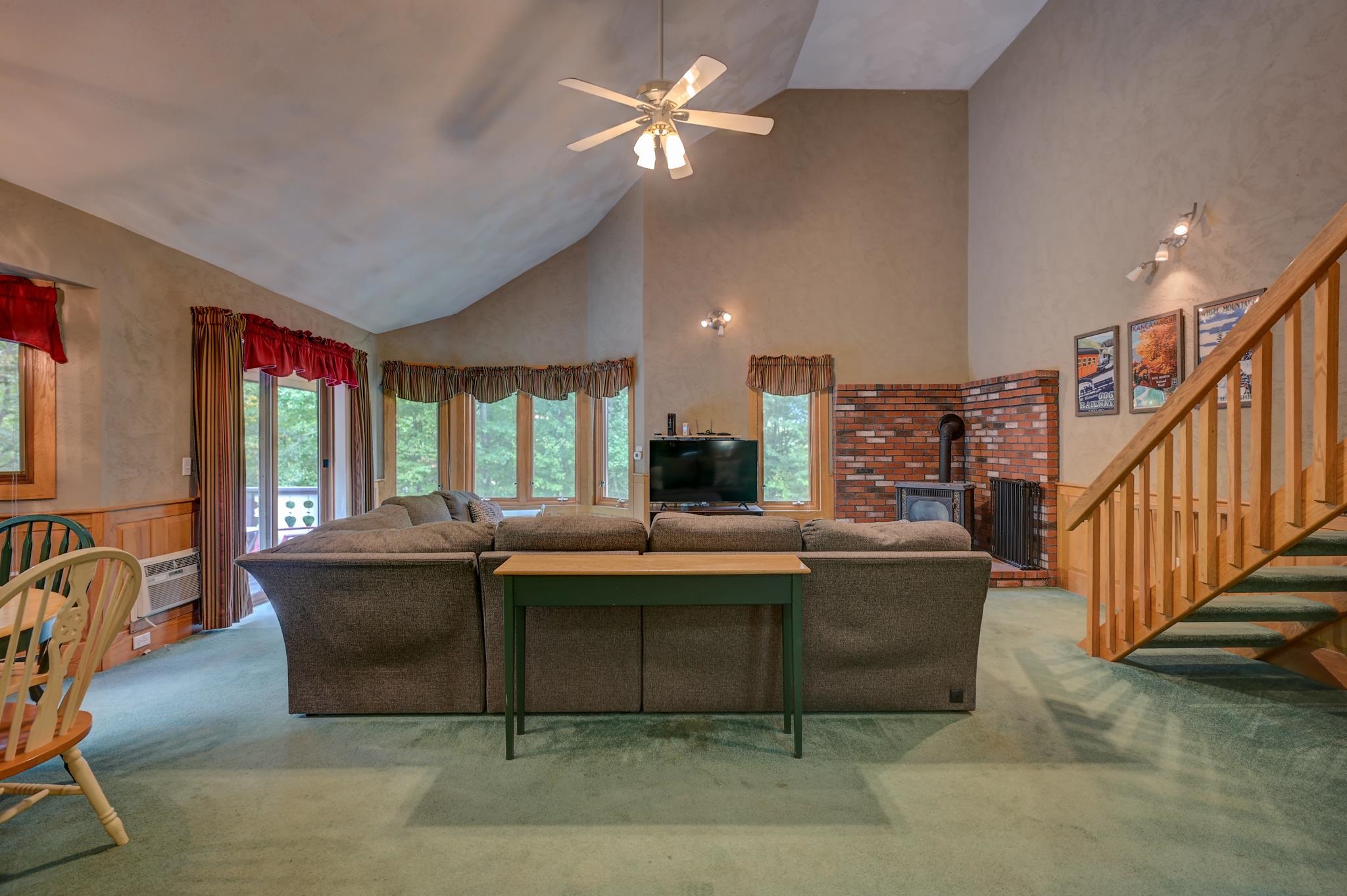 Furnished living room with a vaulted ceiling, brick fireplace, sectional sofa, and wooden staircase.