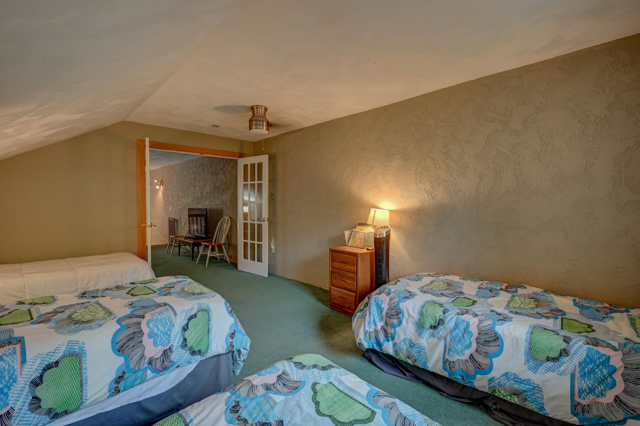 Attic bedroom with three patterned beds, green carpet, and an adjoining sitting area.