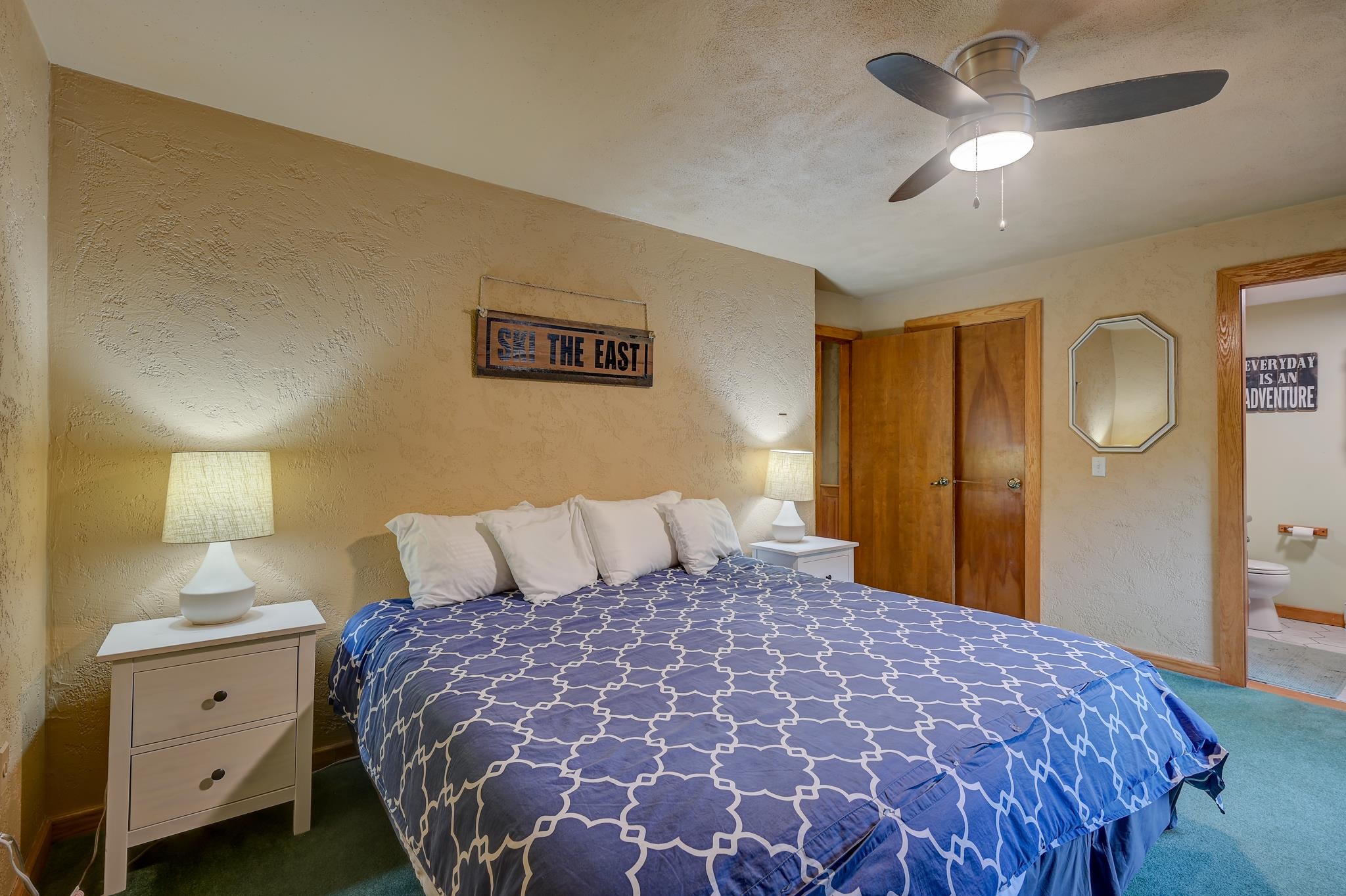 Furnished bedroom with blue patterned bedding, a ceiling fan, and an open doorway to the bathroom.