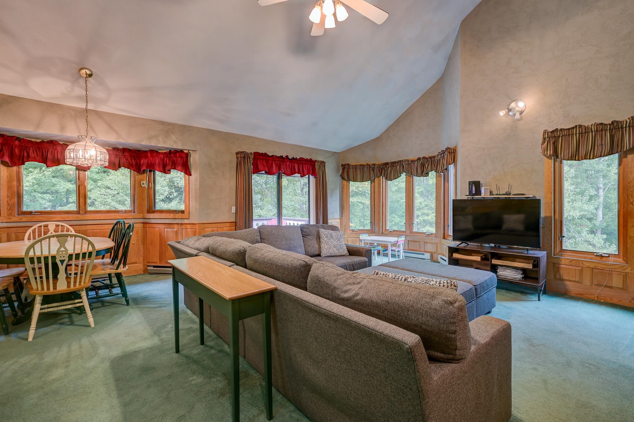 Living room with a vaulted ceiling, large windows, sectional sofa, and adjoining dining area.