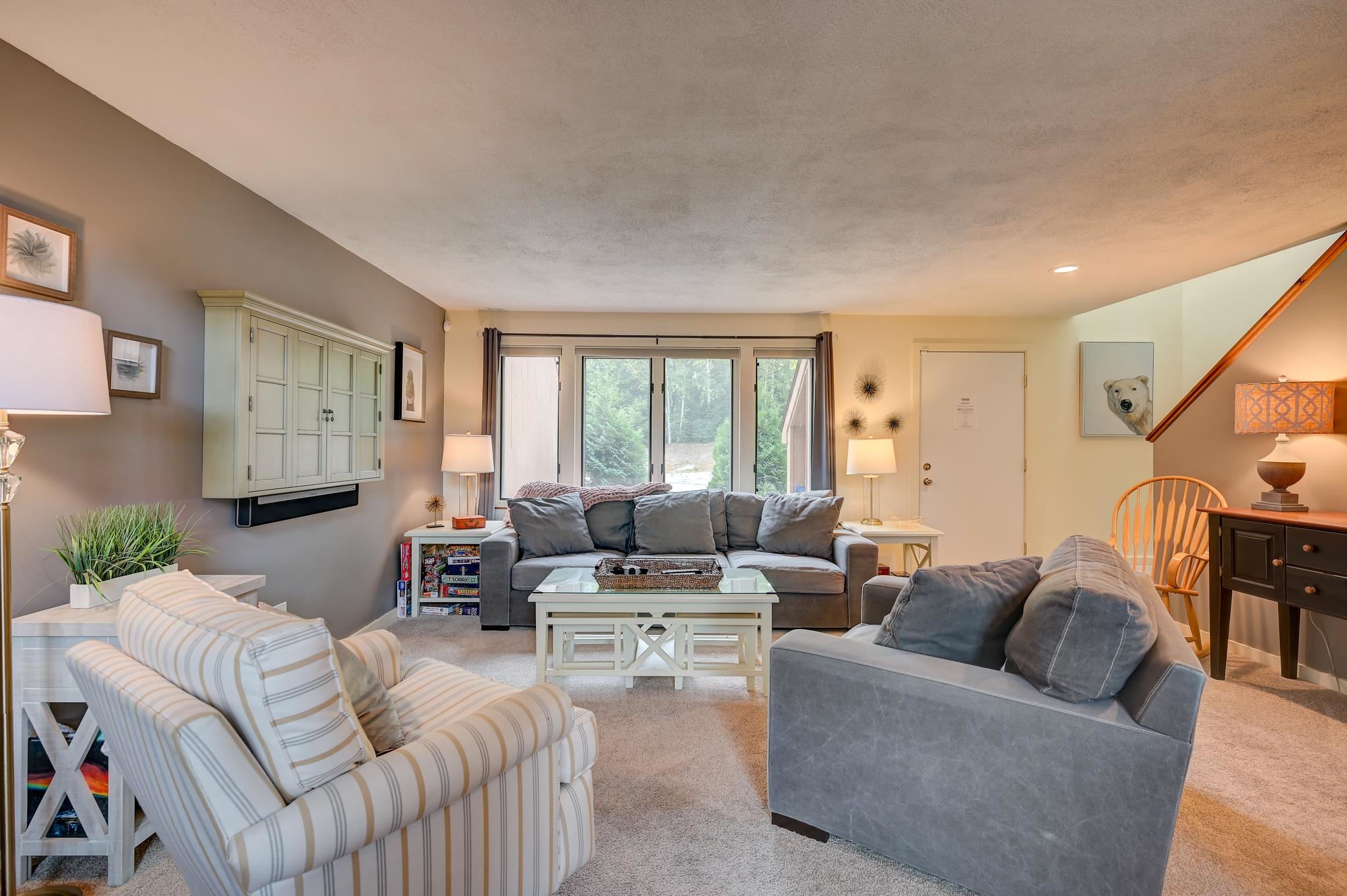 Living room with gray sofas, a striped armchair, and large windows overlooking greenery.
