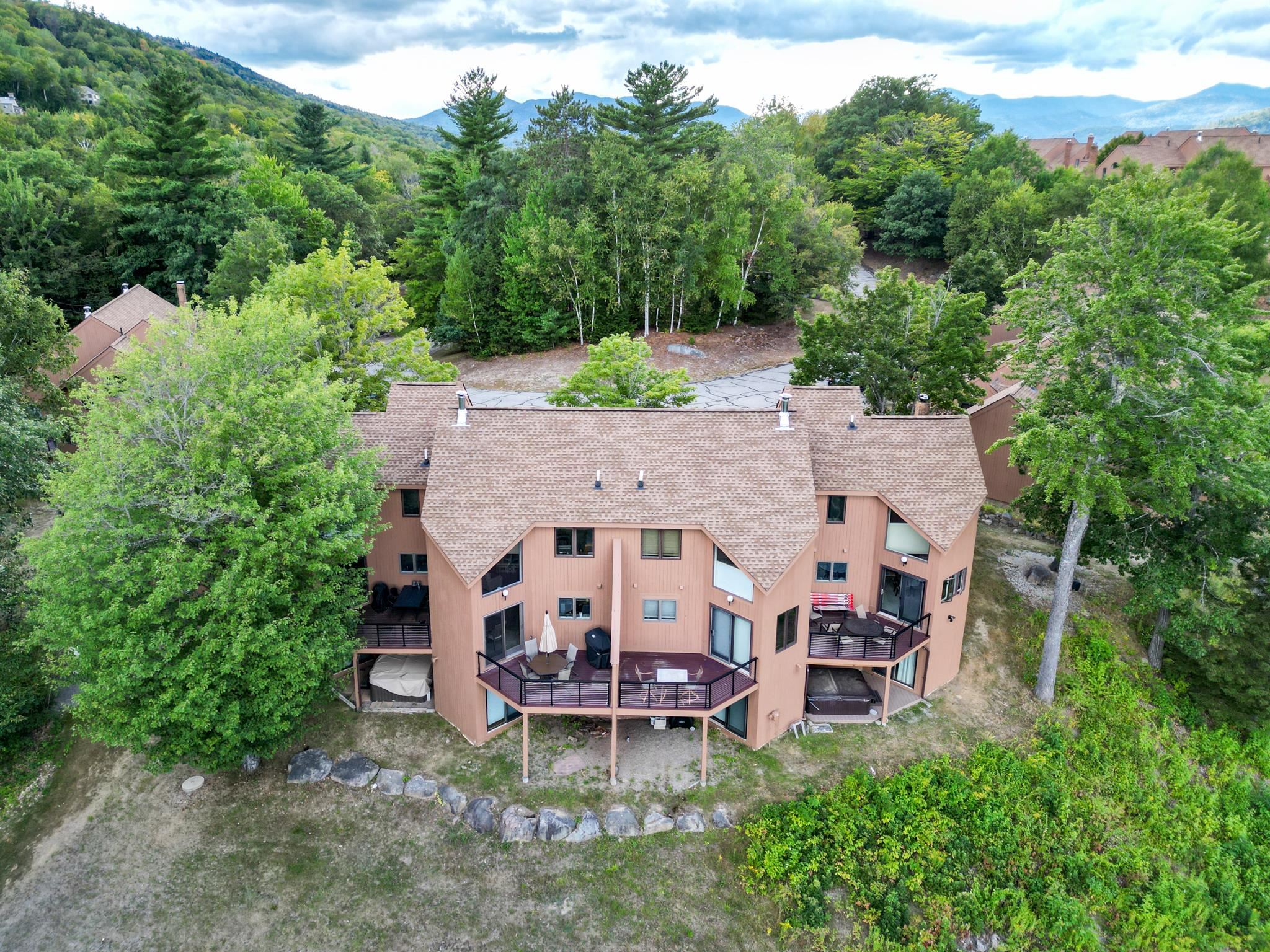 Aerial view of a tan condominium building with raised decks, surrounded by trees and backed by a mountain ridge.