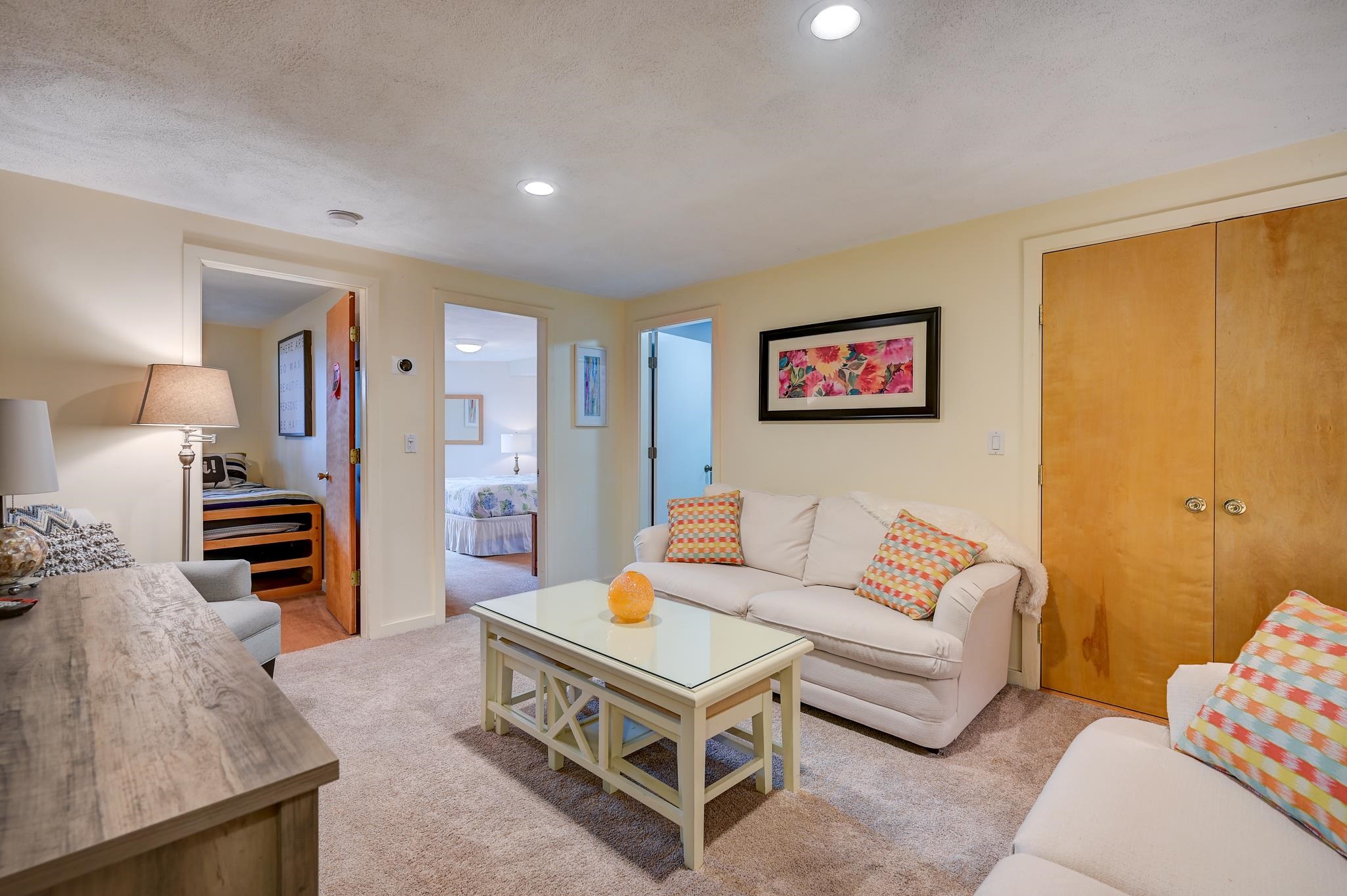 Furnished living room with cream sofas, a glass-top coffee table, and open bedroom doorways.