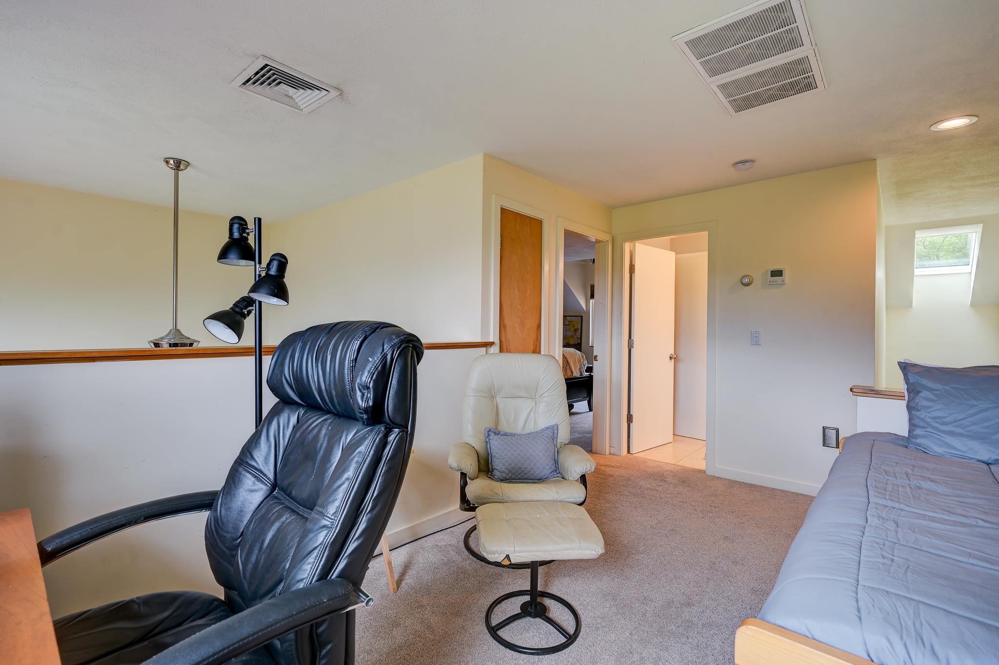 Furnished bedroom with a blue bed and two chairs beneath a sloped ceiling.
