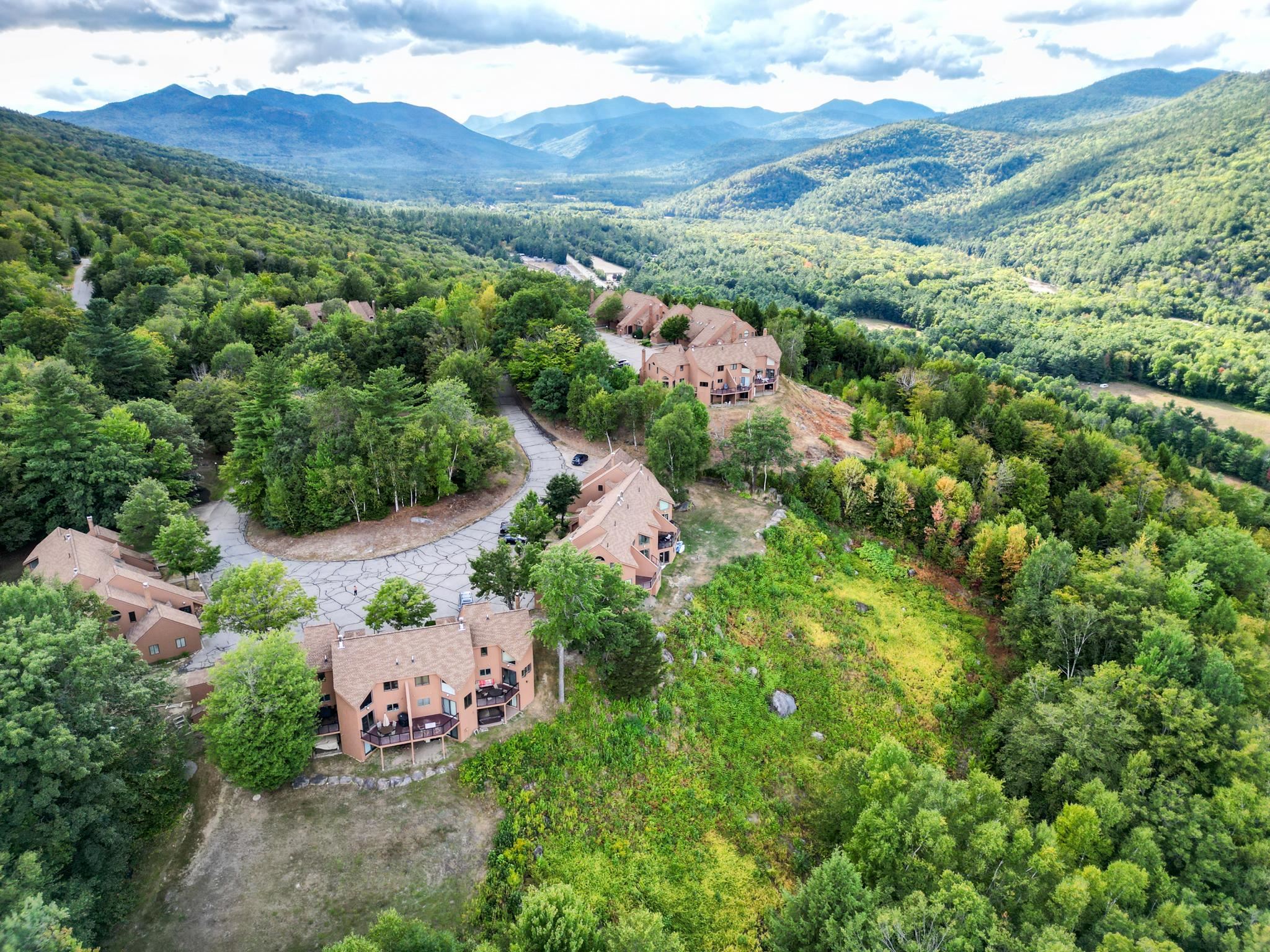 Aerial view of forested condominiums, winding driveway, and distant mountain ranges.