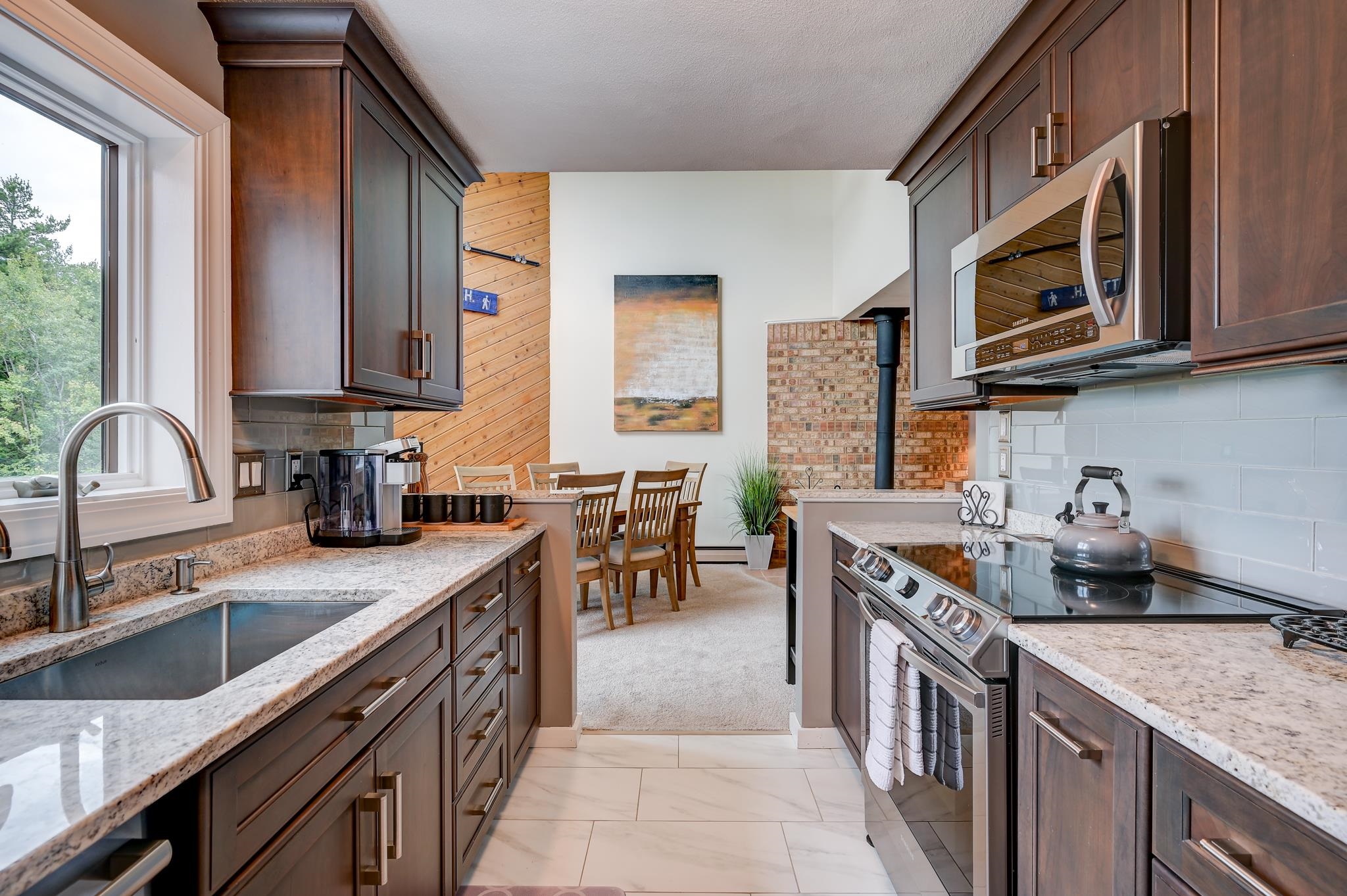 Kitchen with dark wood cabinets, granite counters, stainless appliances, and a dining area beyond.