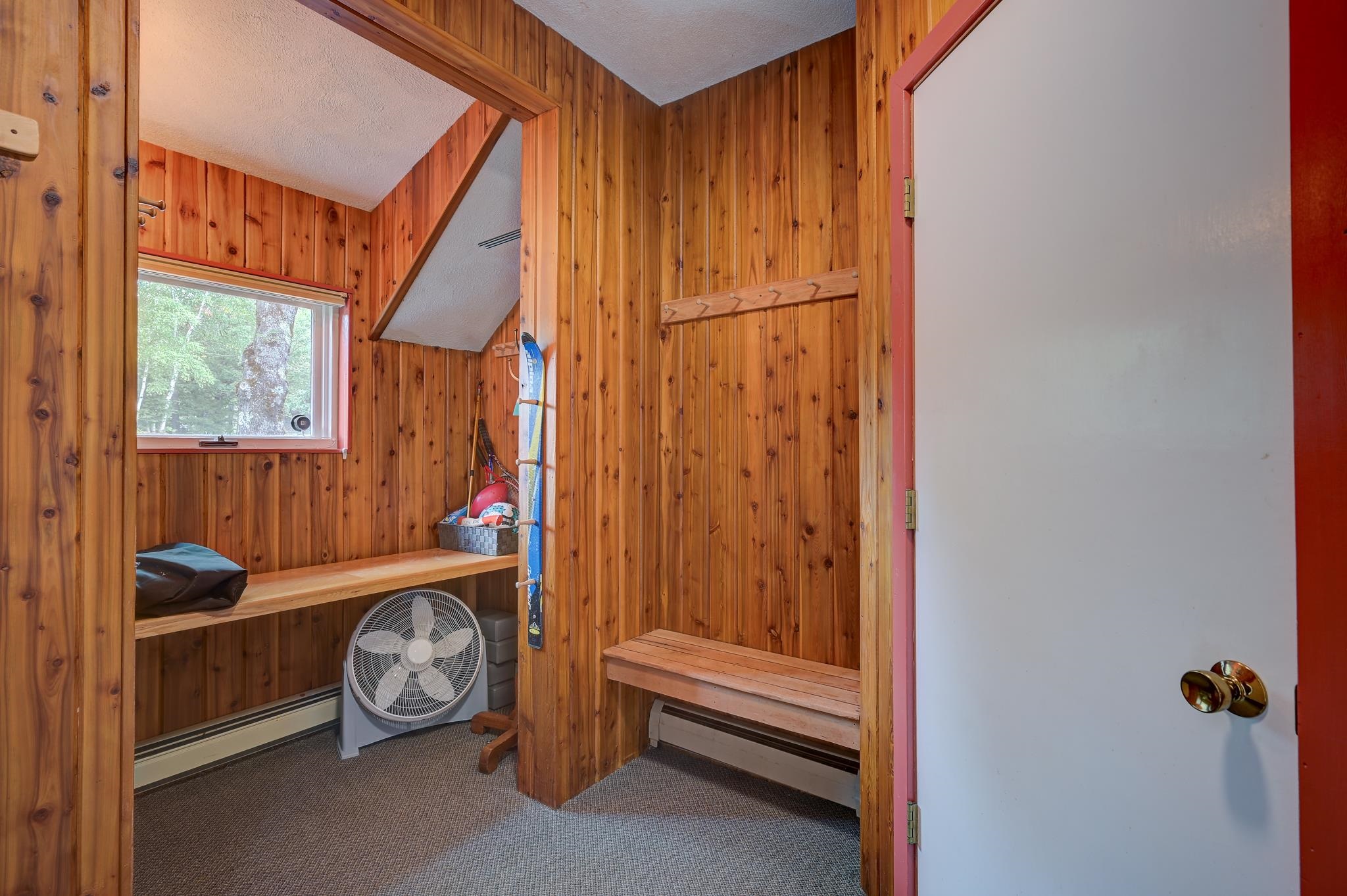 Wood-paneled room with built-in benches, coat hooks, a window, and stored outdoor gear.