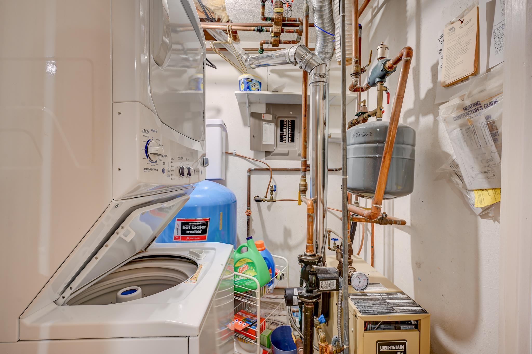 Laundry and mechanical room with an open washer, hot water tank, boiler, and exposed pipes.
