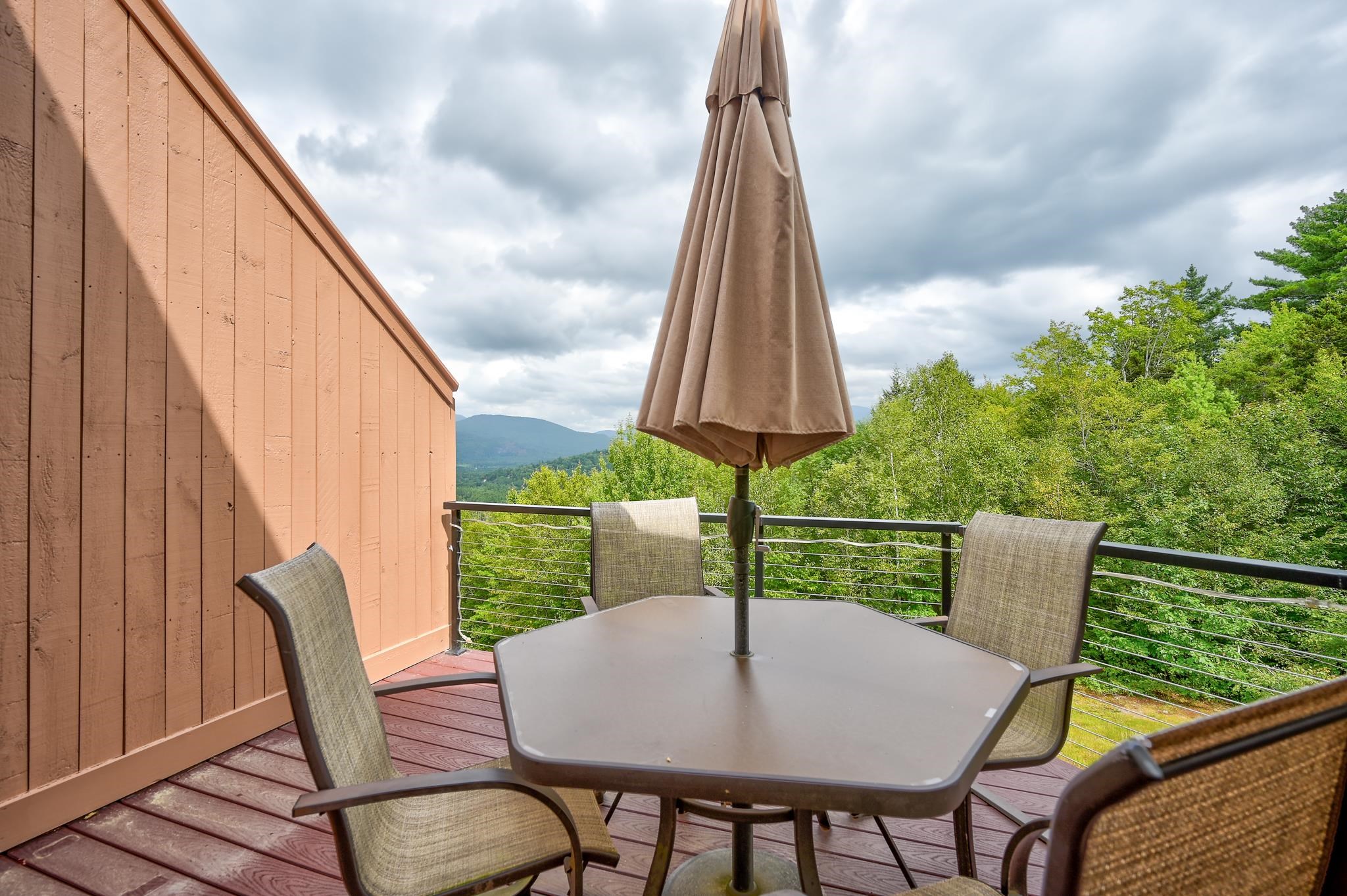 Deck dining area with mountain views, cable railing, and a closed patio umbrella.