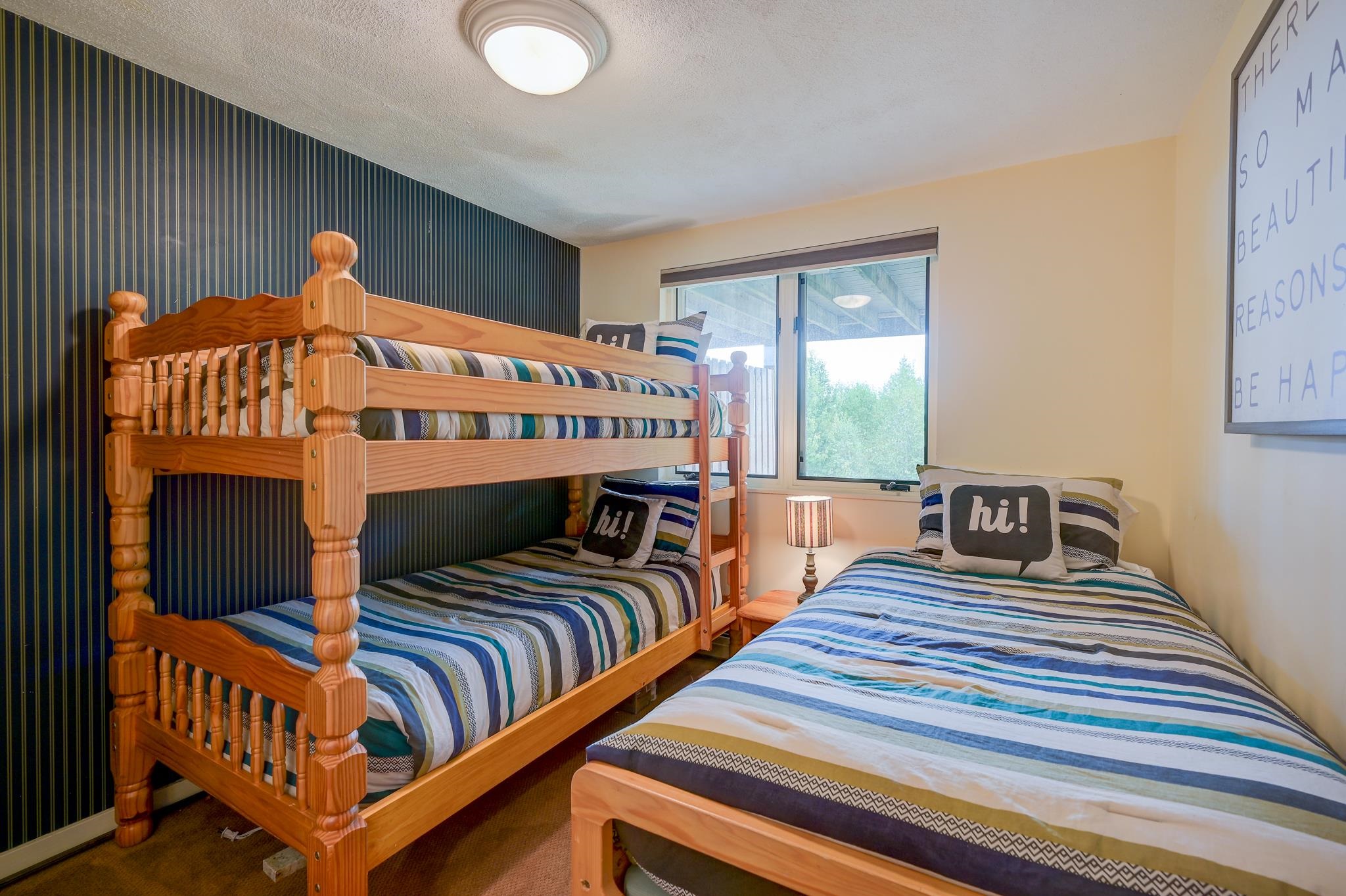 Bedroom with a wooden bunk bed beside a separate bed, both dressed in striped bedding.