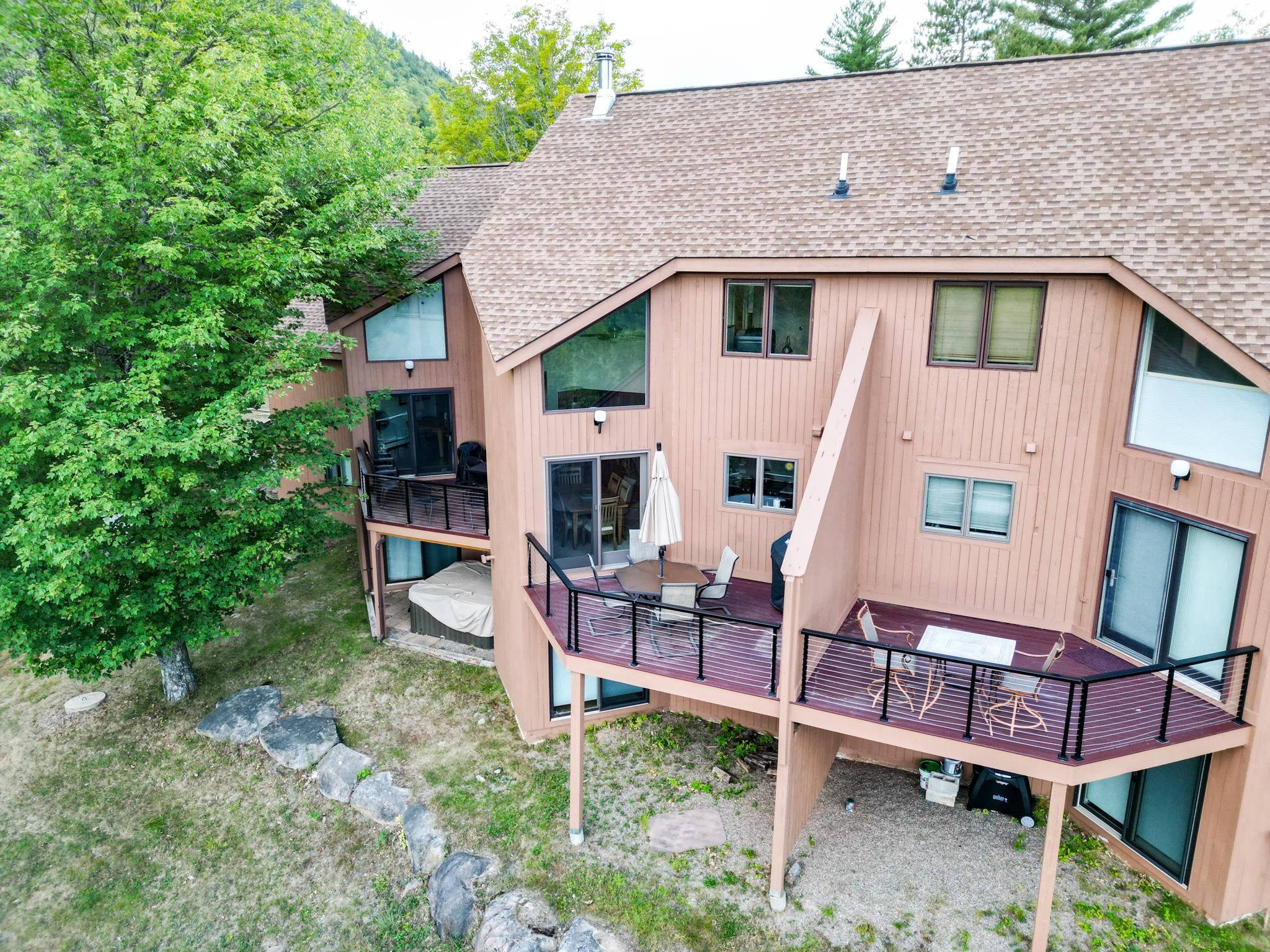 Condominium exterior with raised decks, outdoor seating, and mature trees.