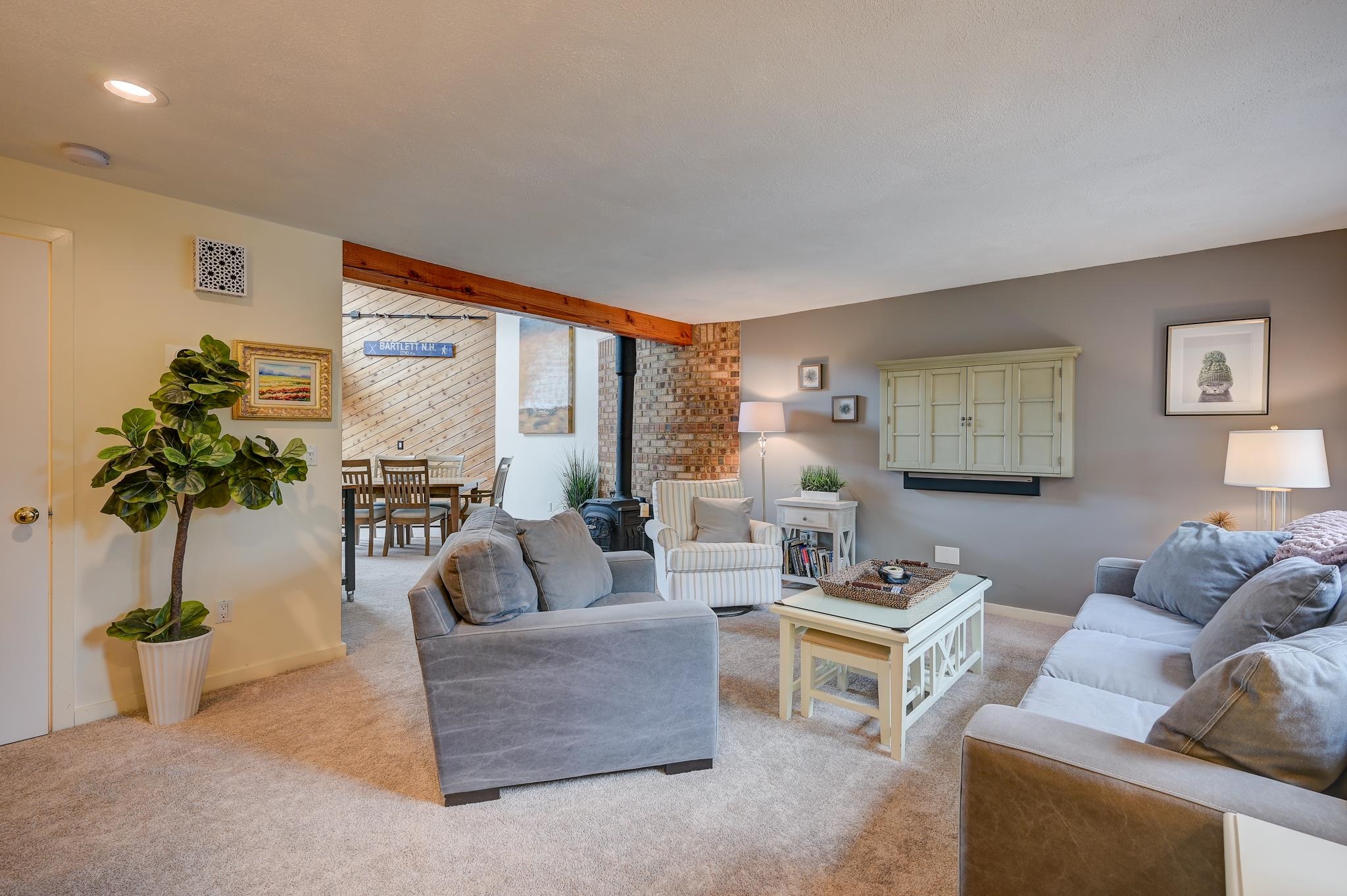 Furnished living room with gray sofas, a brick fireplace, and an adjoining dining area.