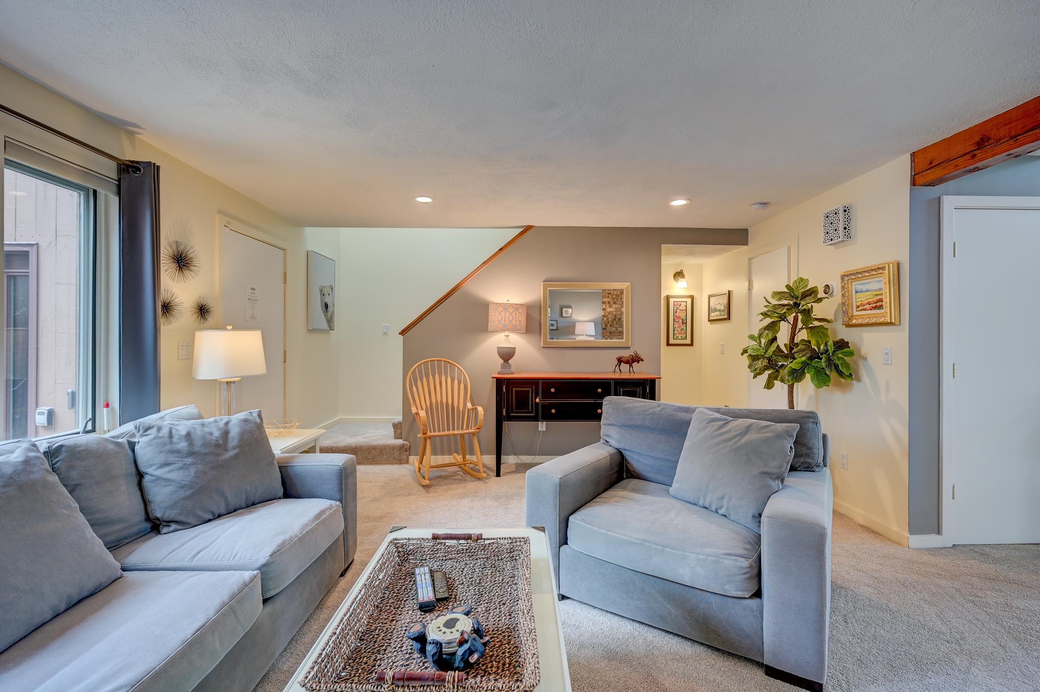 Staged living room with blue-gray sofas, a wooden rocking chair, and stairs.