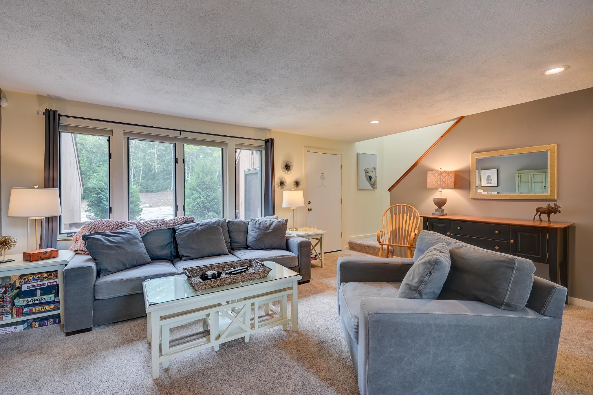Furnished living room with blue-gray sofas, large windows, and a staircase.