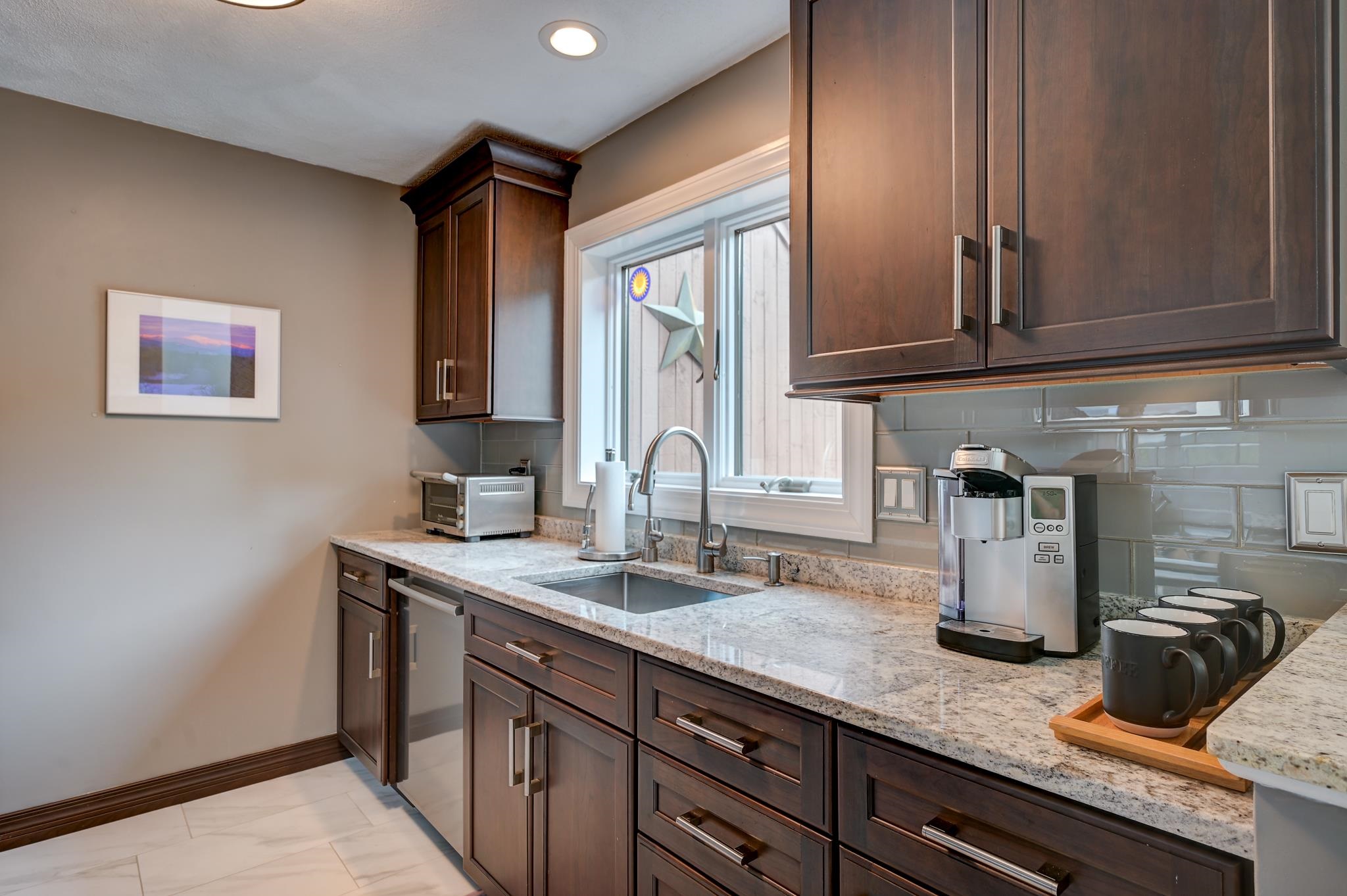 Kitchen with dark wood cabinets, stone counters, and a sink beneath a window.