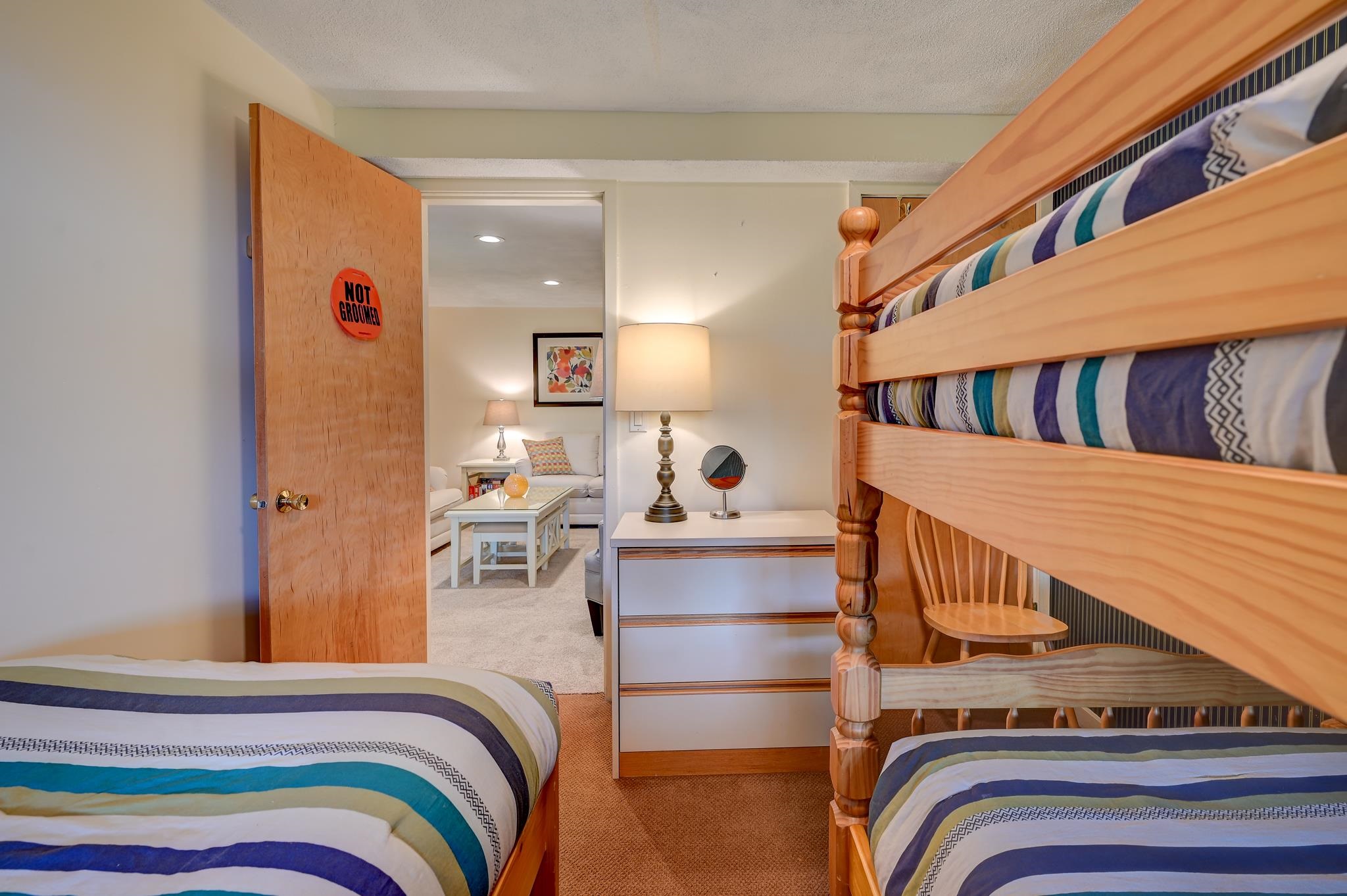 Bedroom with striped bedding, a wooden bunk bed, and a doorway leading to a sitting area.