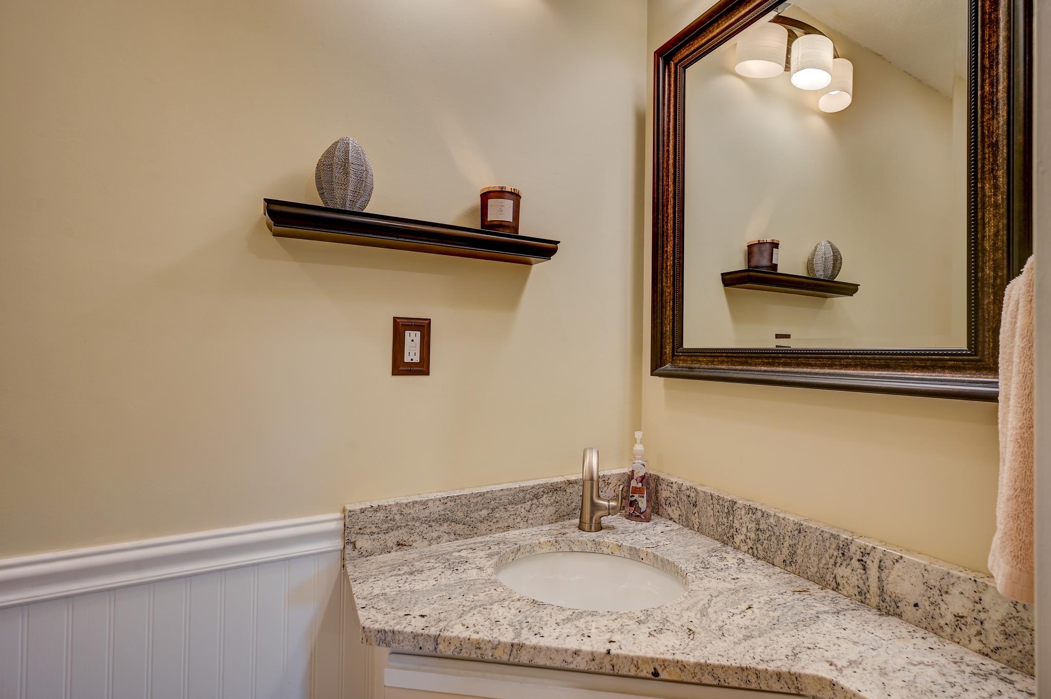 Bathroom vanity with a speckled granite counter, oval sink, bronze faucet, and large framed mirror.