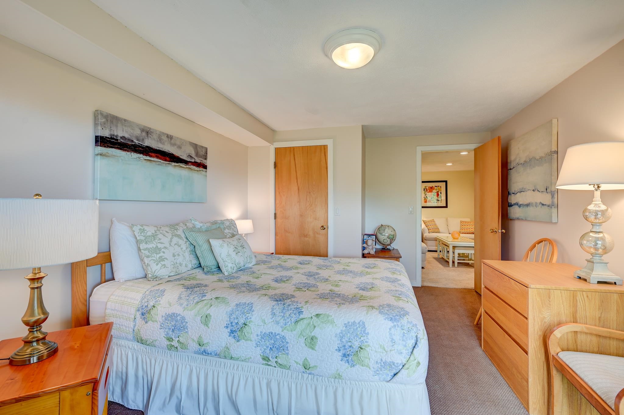 Furnished bedroom with a blue floral quilt, wooden furniture, and an open doorway to a sitting room.