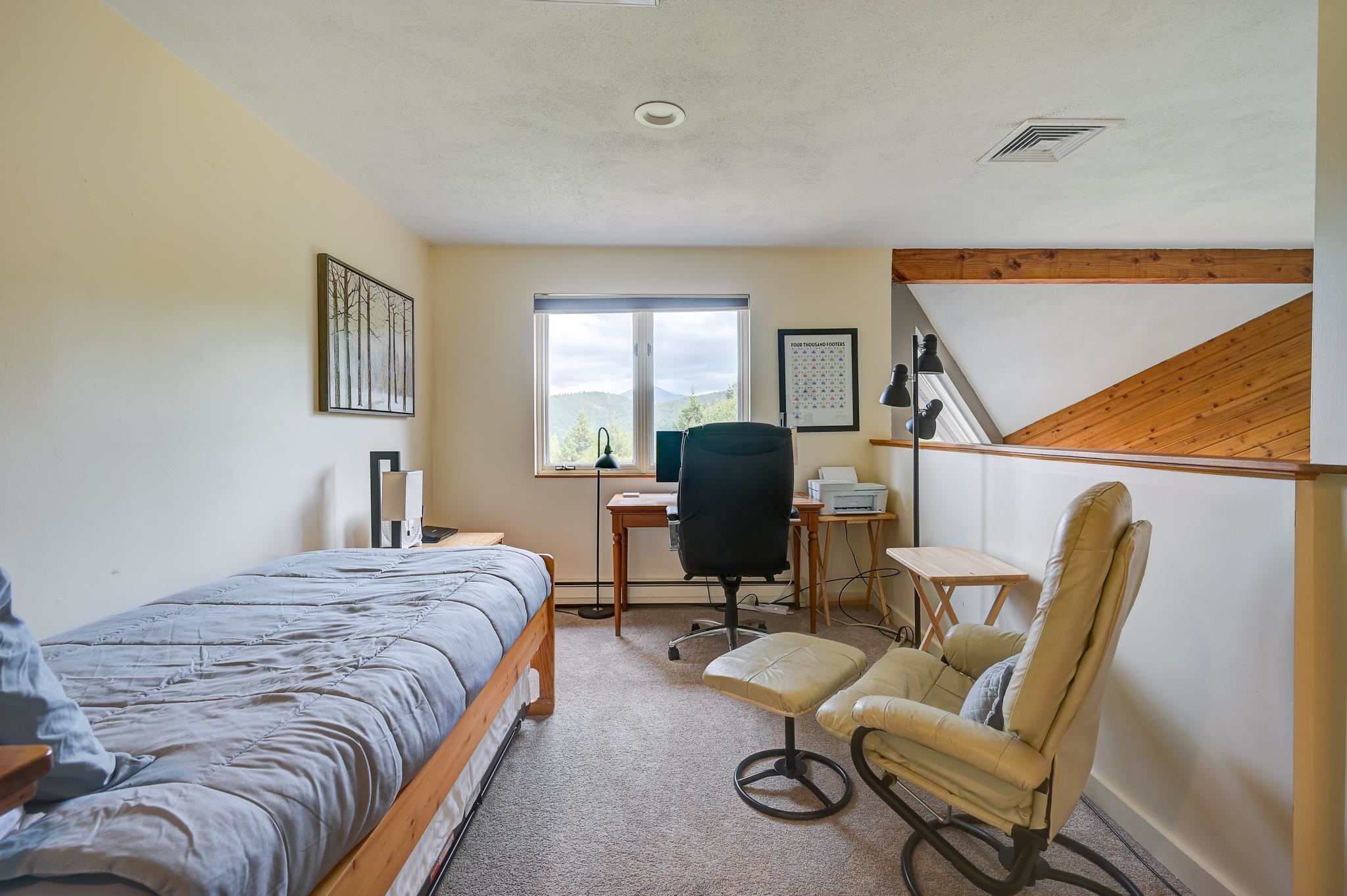 Bedroom office with a single bed, desk, recliner, and forested mountain views through the window.