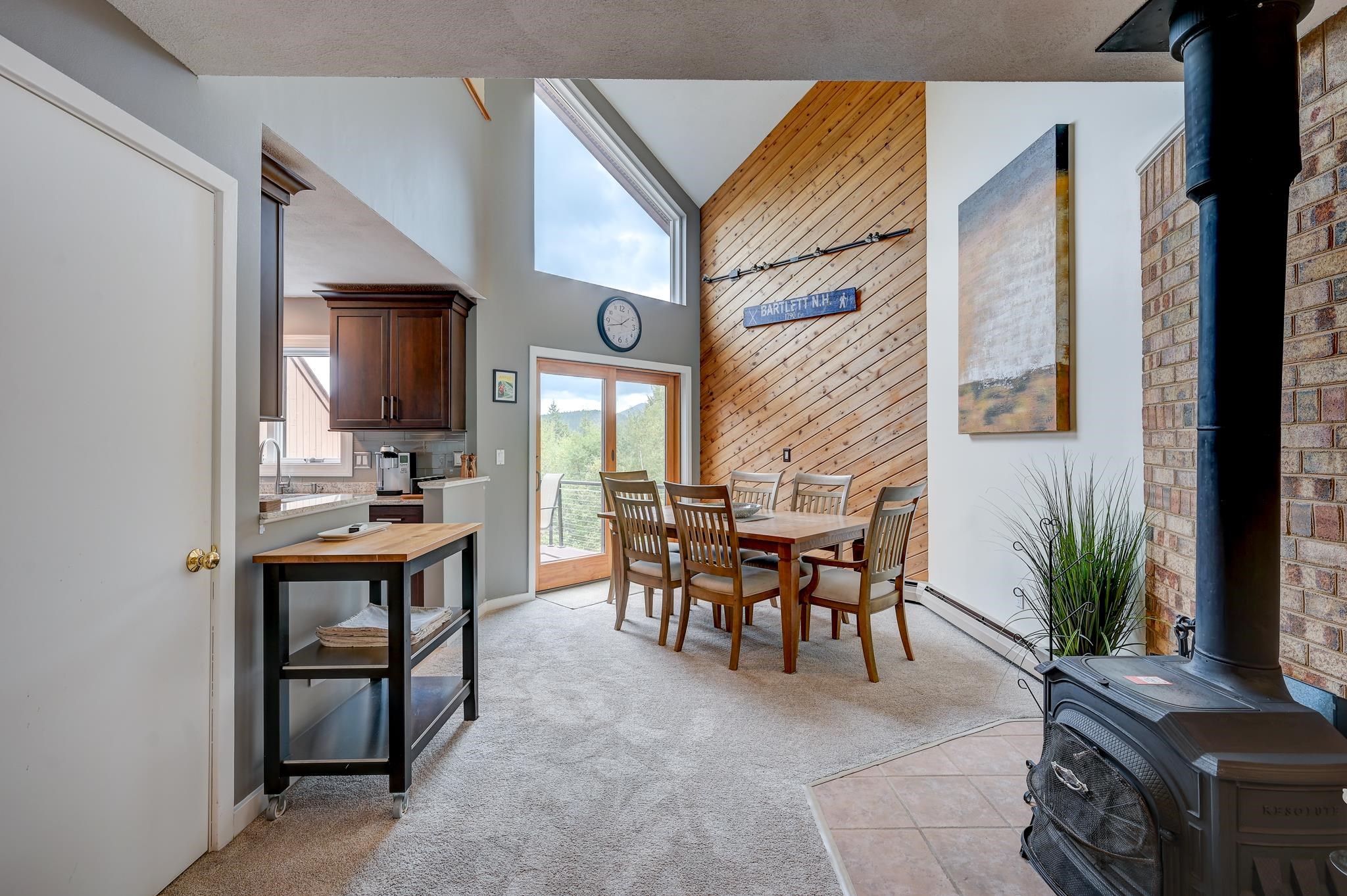Dining area with a vaulted wood-plank wall, mountain views through large windows, and a black wood stove.