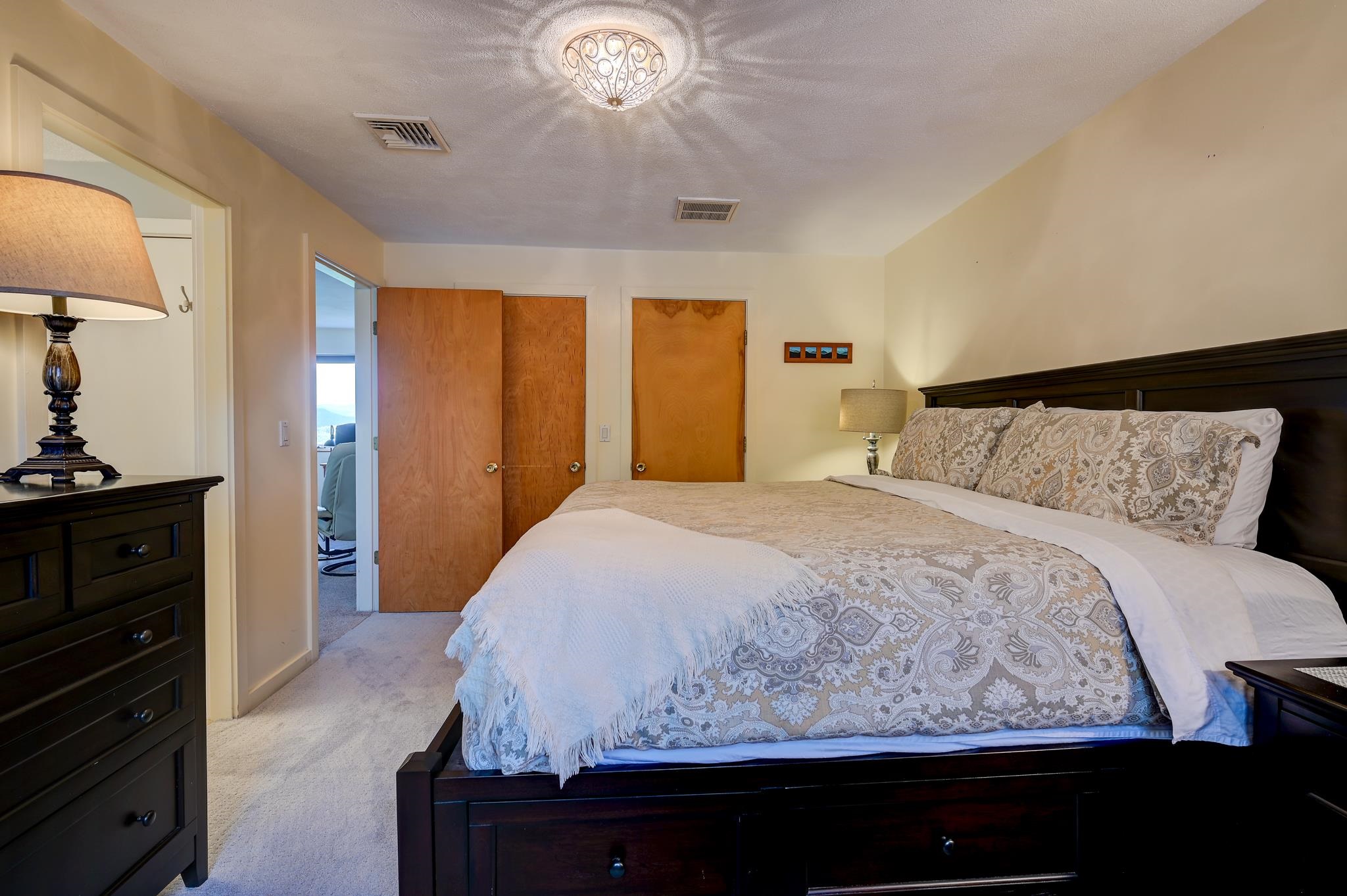 Furnished bedroom with a dark wood bed and patterned bedding; open doors lead to an adjoining room.