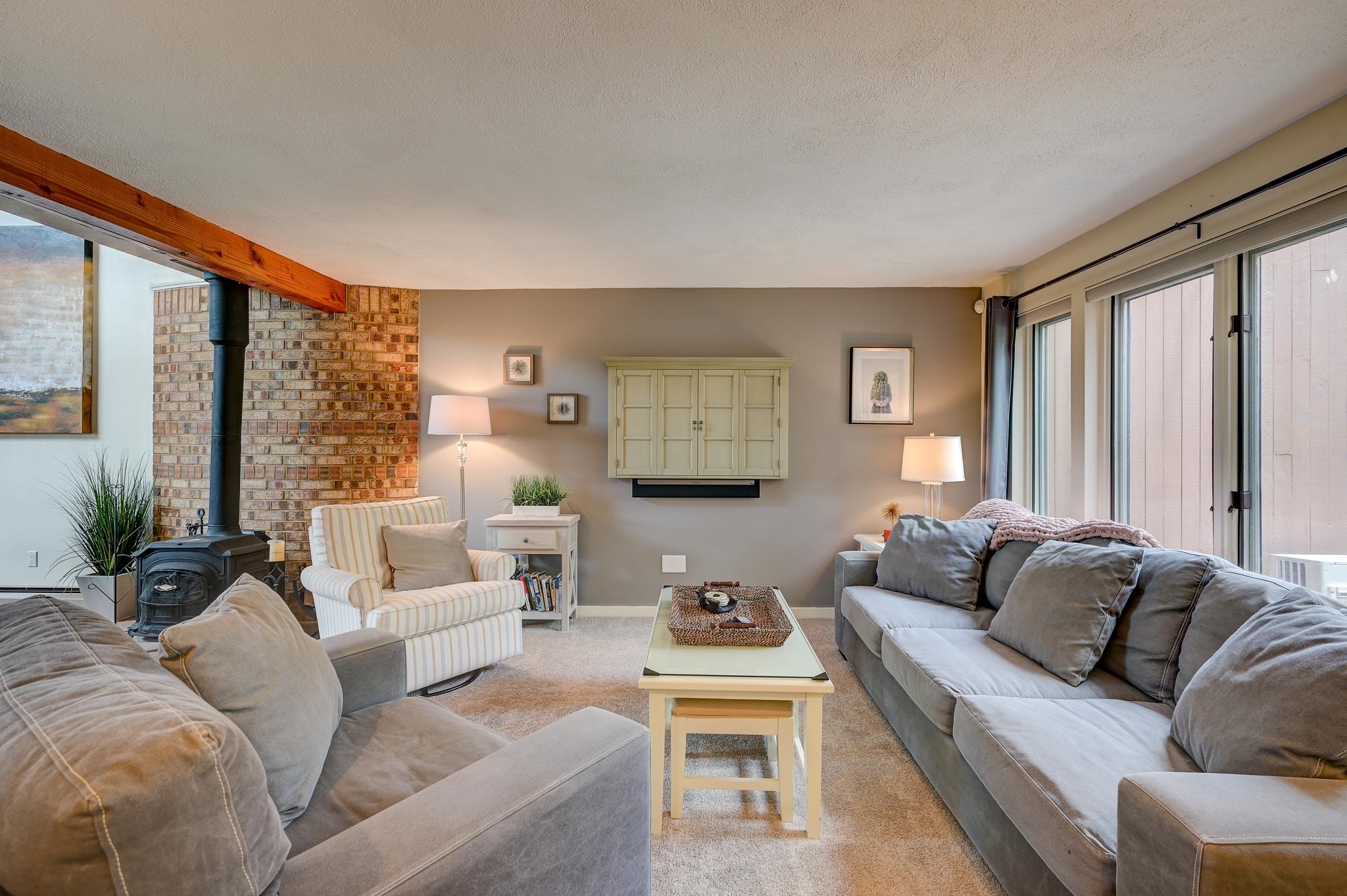 Living room with gray sofas, a brick wall, and a black wood stove.