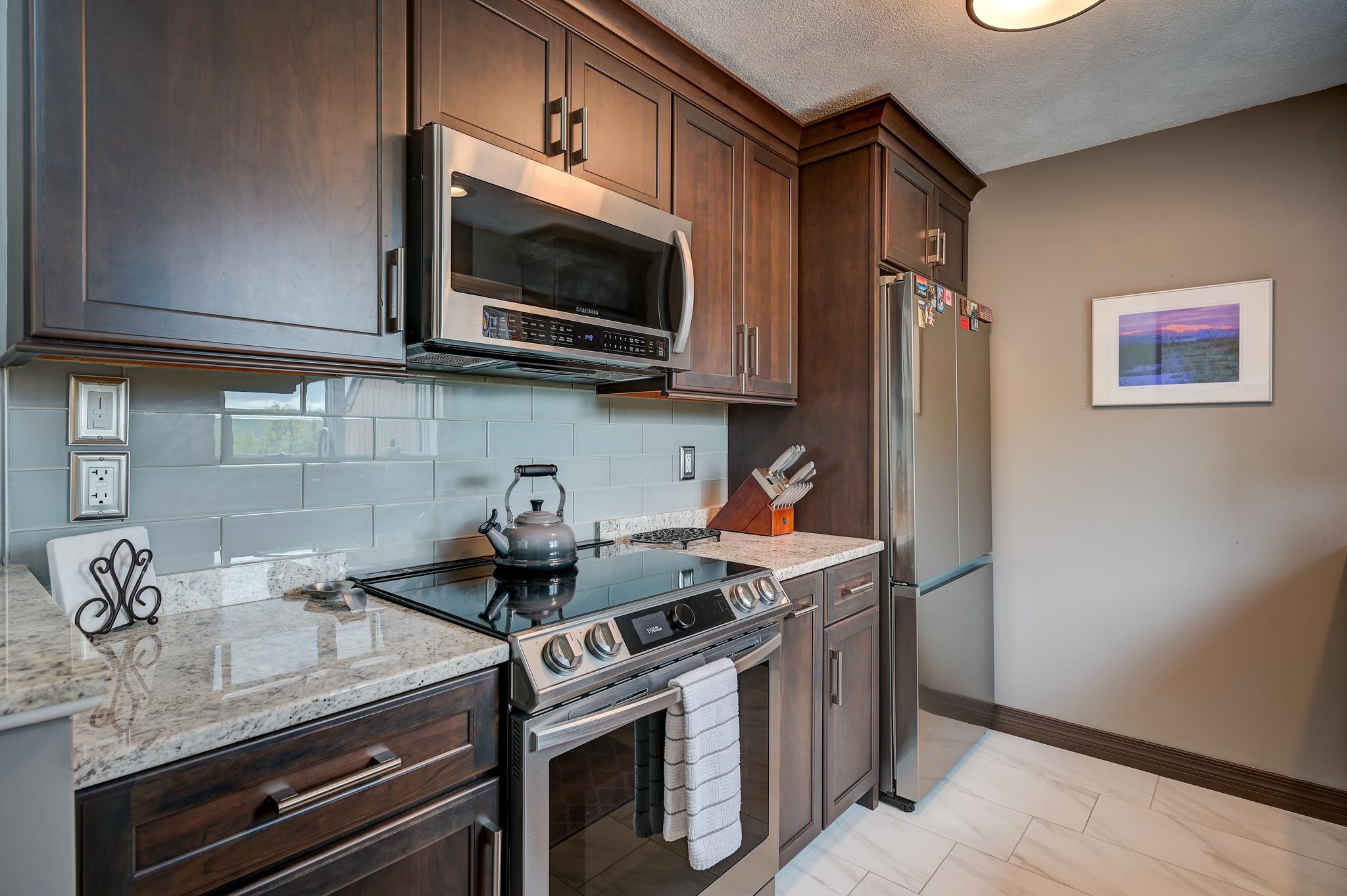 Kitchen with dark wood cabinets, pale blue tile backsplash, granite counters, and stainless steel appliances.