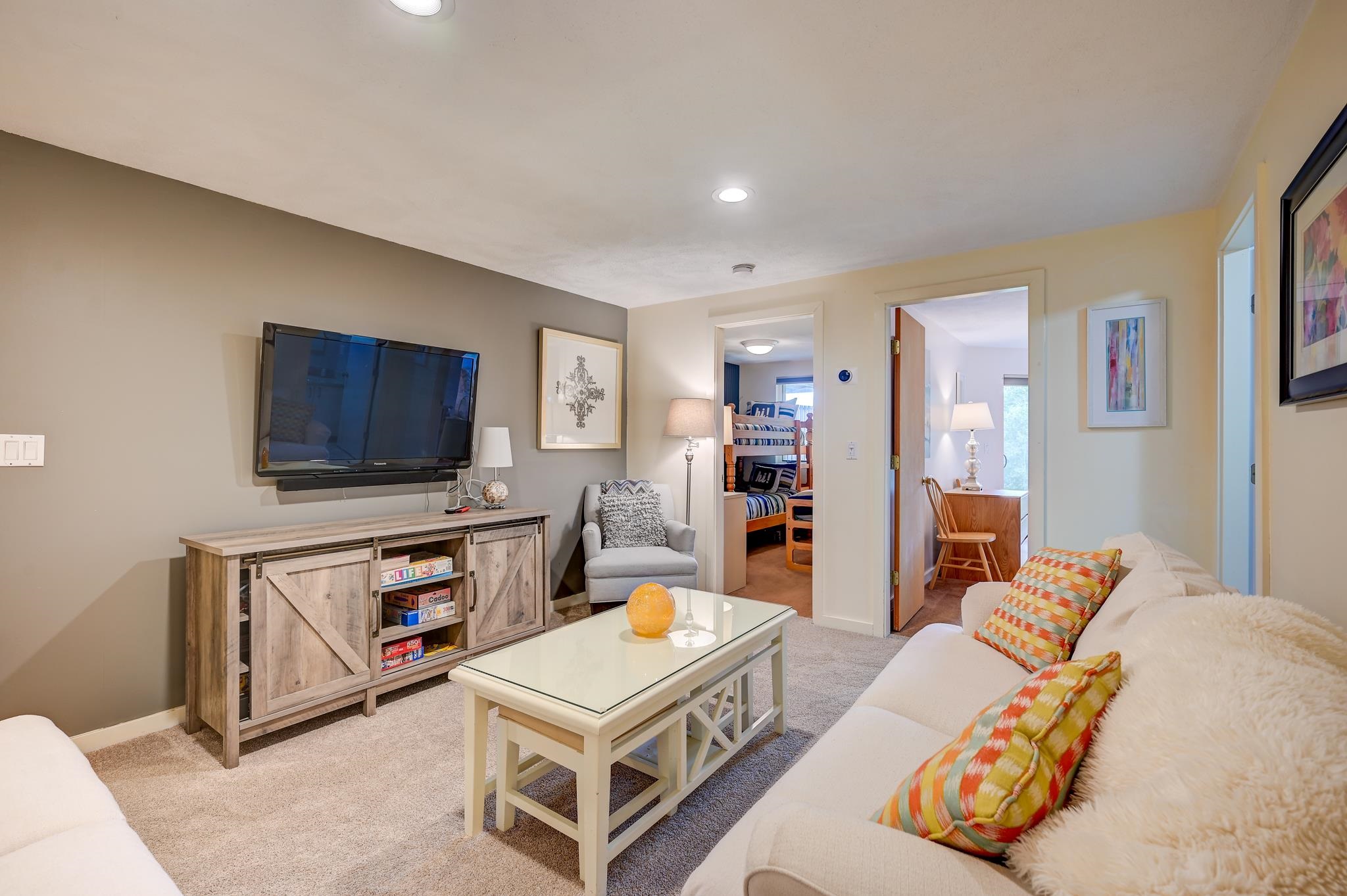 Furnished living room with a wall-mounted TV, glass coffee table, and open doorway to a bunk room.