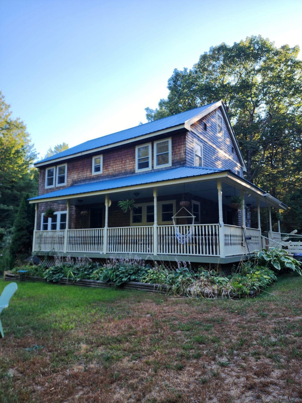Two-story shingle-sided home with a blue metal roof and wide covered porch.